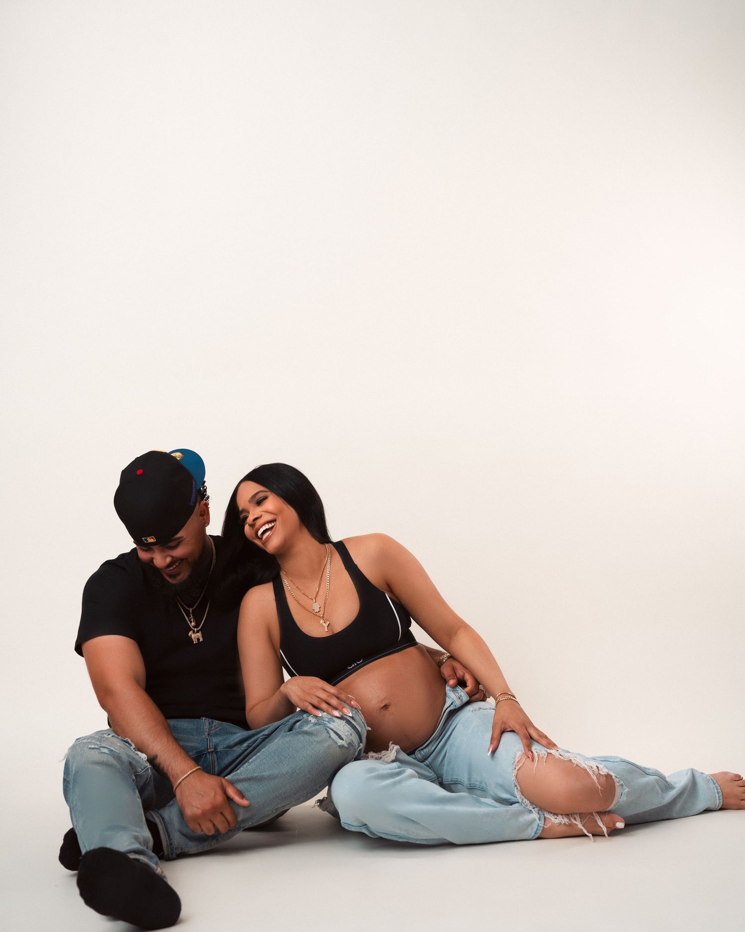 Couple in black outfits and blue jeans lay together intimately on white backdrop in artistic photo series.
