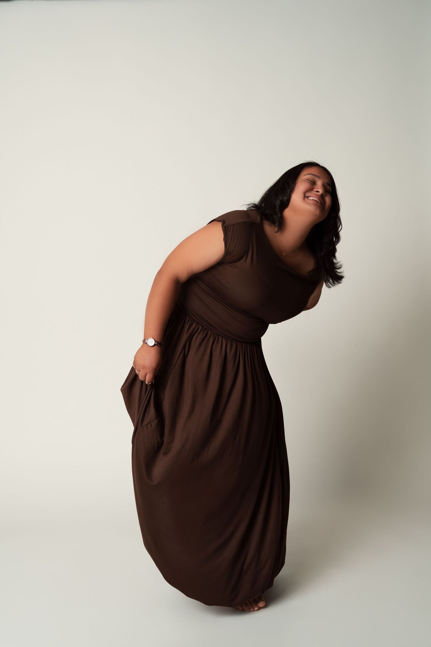 Four sequential photos of a person wearing a brown dress curling into a compact ball shape against a white backdrop.