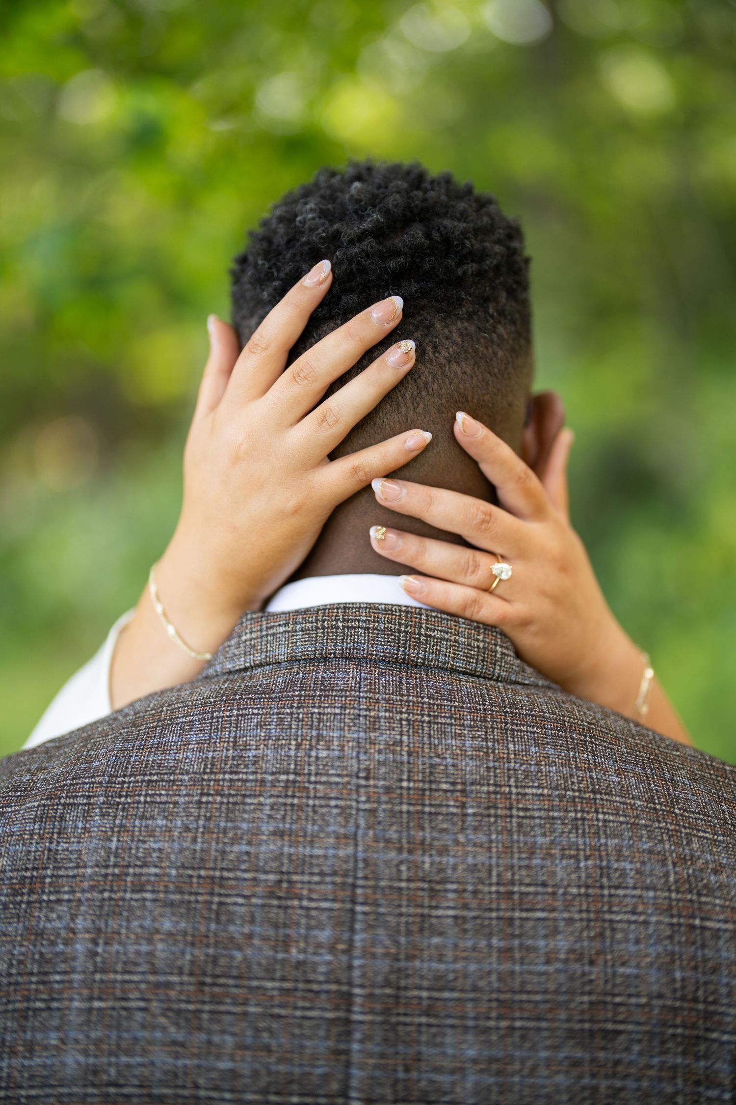 A woman's hand with an engagement ring reaches across to caress someone's back wearing a grey checked jacket.