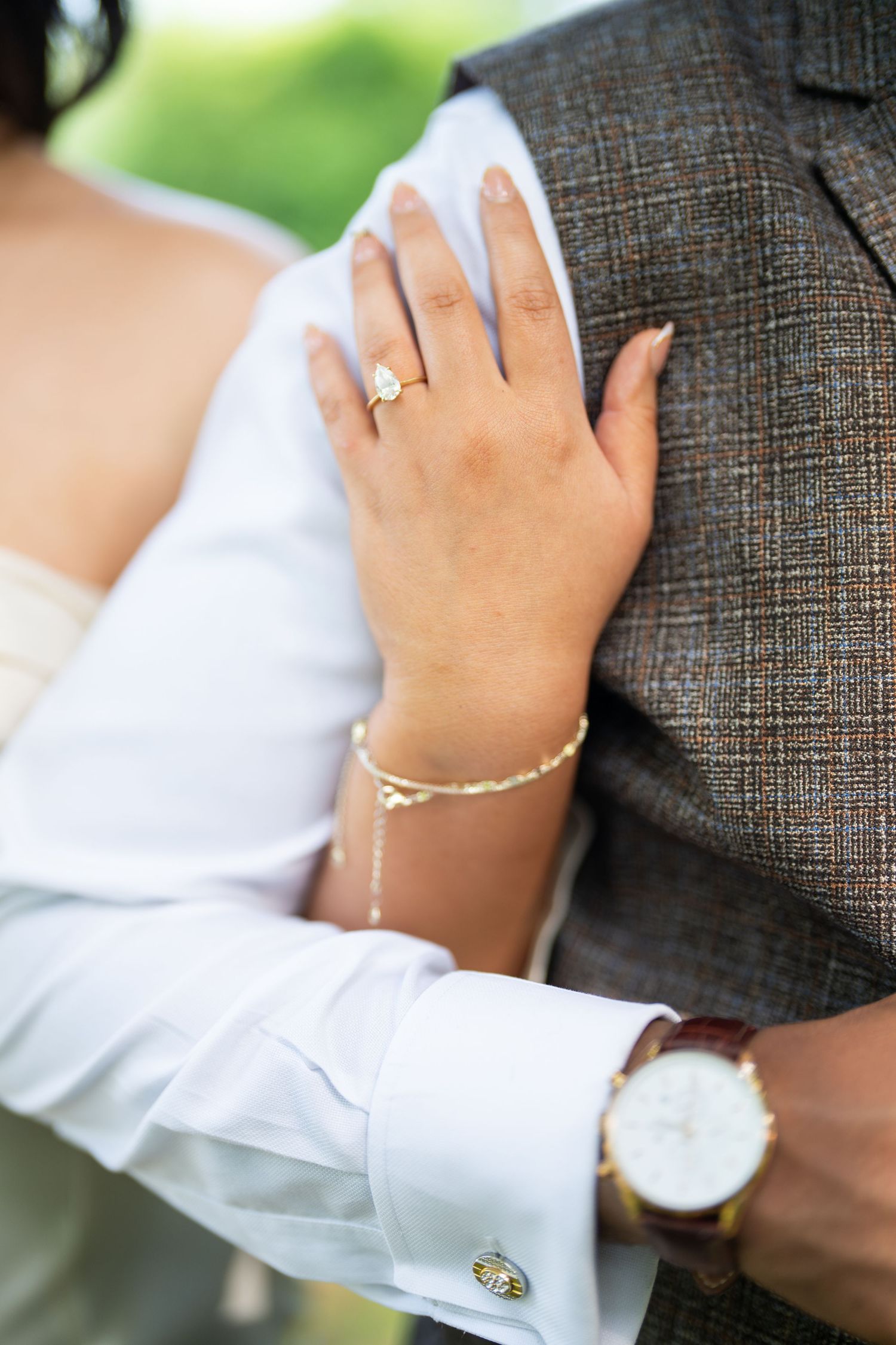 Hands wearing wedding rings and jewelry shown in close-up romantic poses on textured gray fabric.