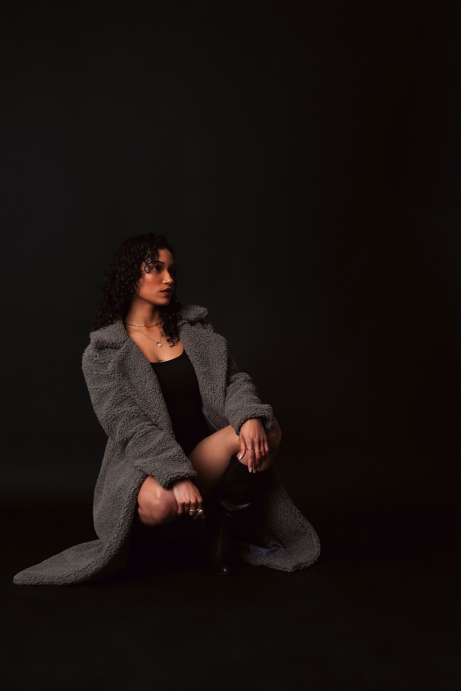 Artistic portrait in darkness showing figure in oversized gray sweater in dramatic poses against black background.
