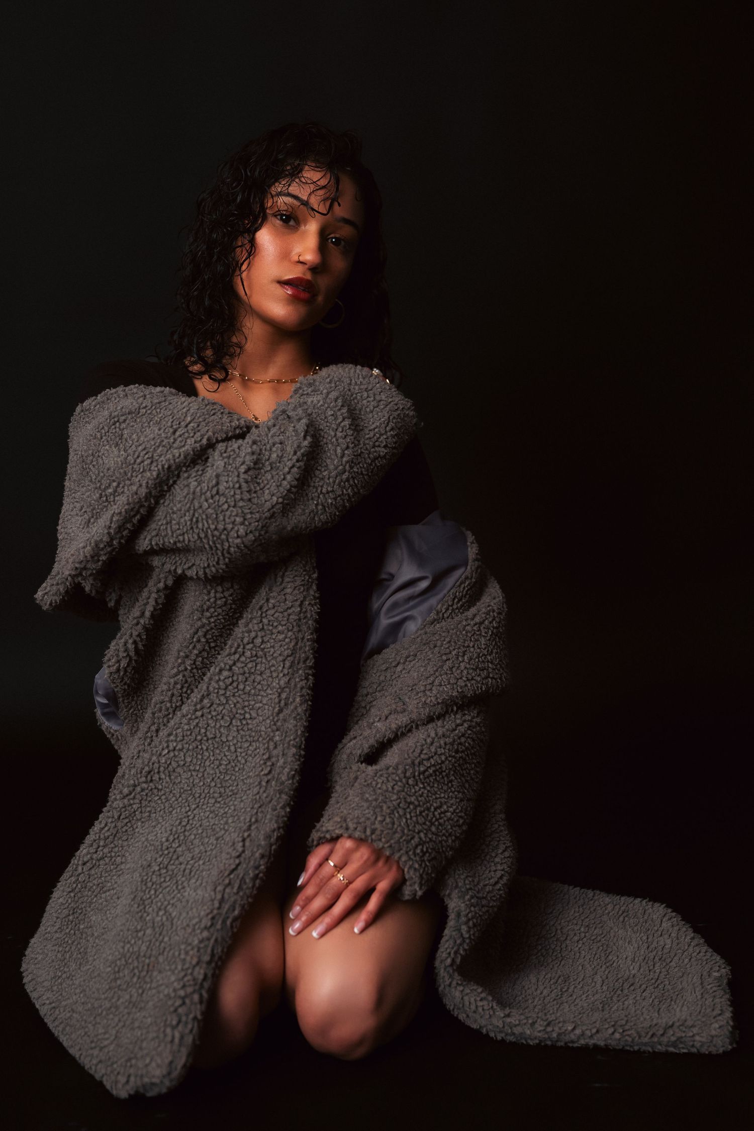 Moody boudoir photoshoot featuring person in chunky knit cardigan posing dramatically in low light.