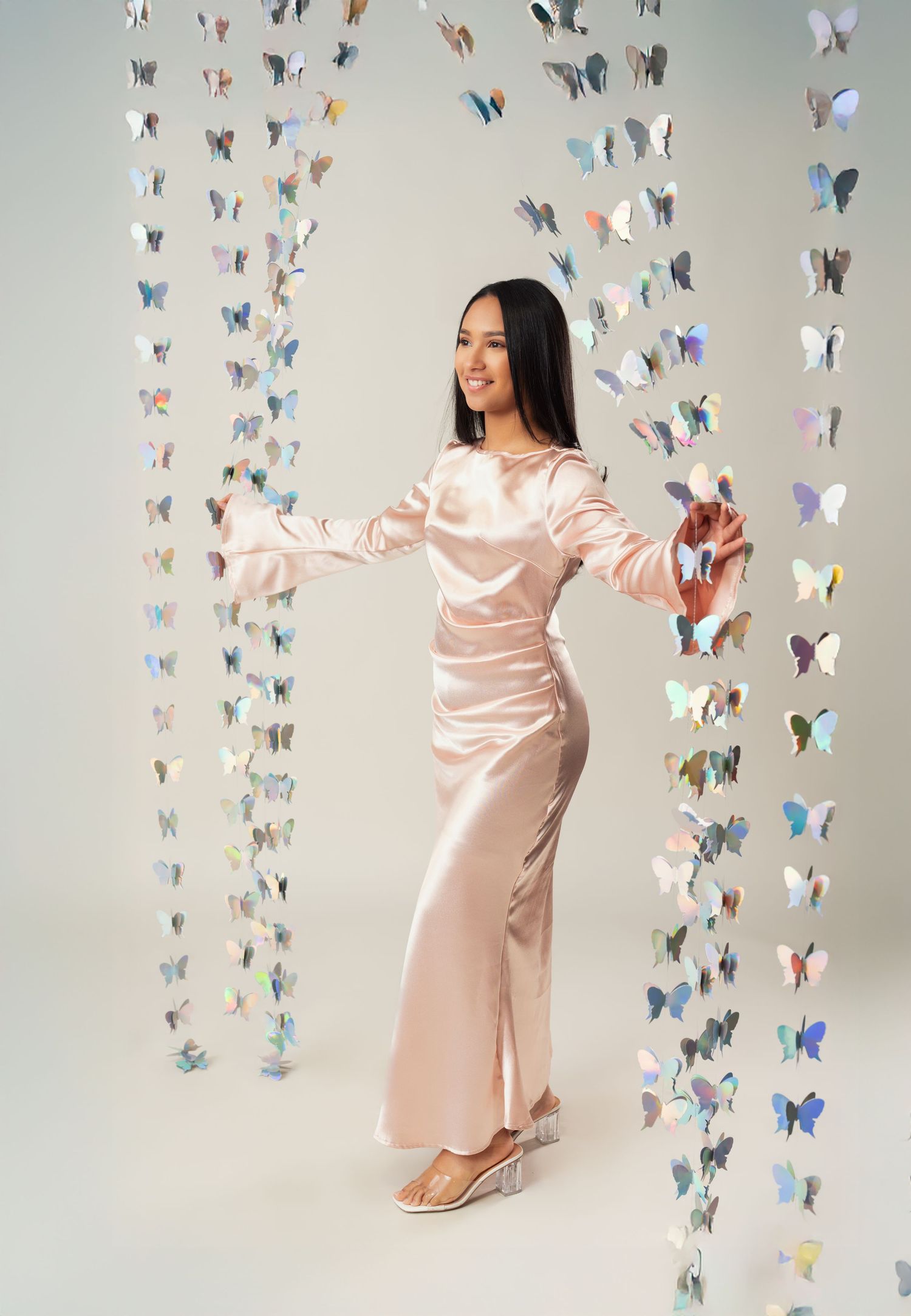 A person in a pink satin dress poses joyfully against a backdrop of colorful paper butterflies in an artistic photo series.