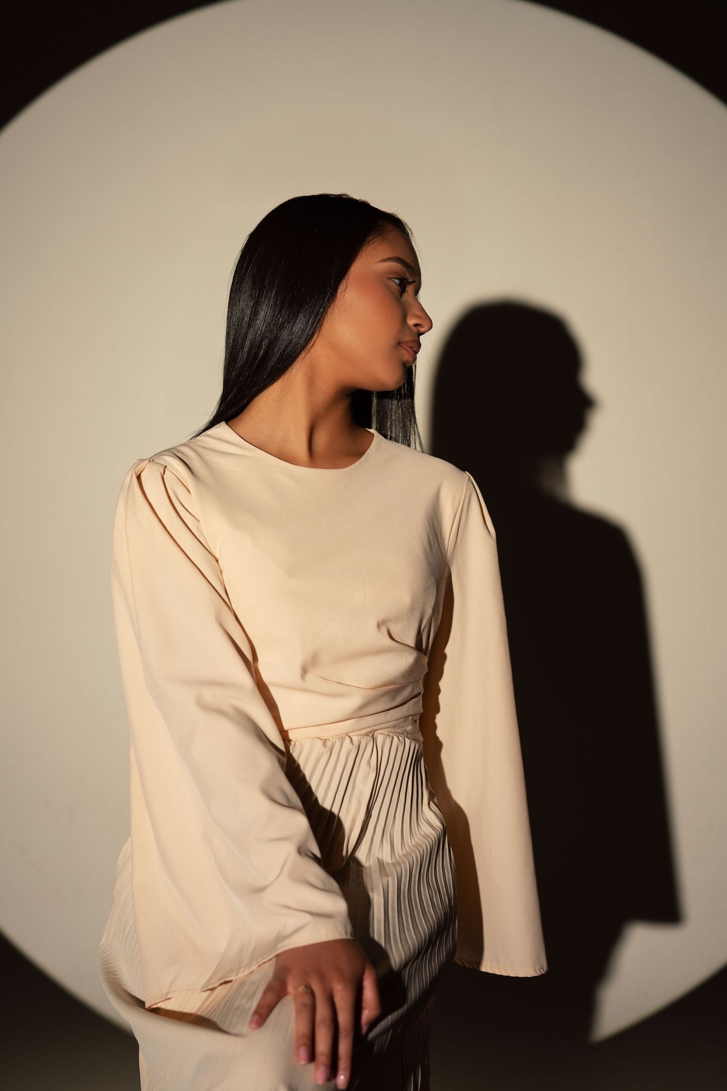 Artistic portrait series showing person in cream dress with dramatic shadow play on beige backdrop.