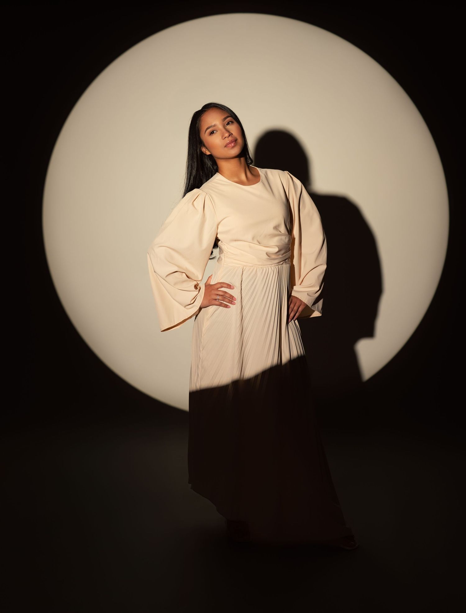 A figure in white flowing sleeves performs elegant movements against a black background with dramatic spotlighting.