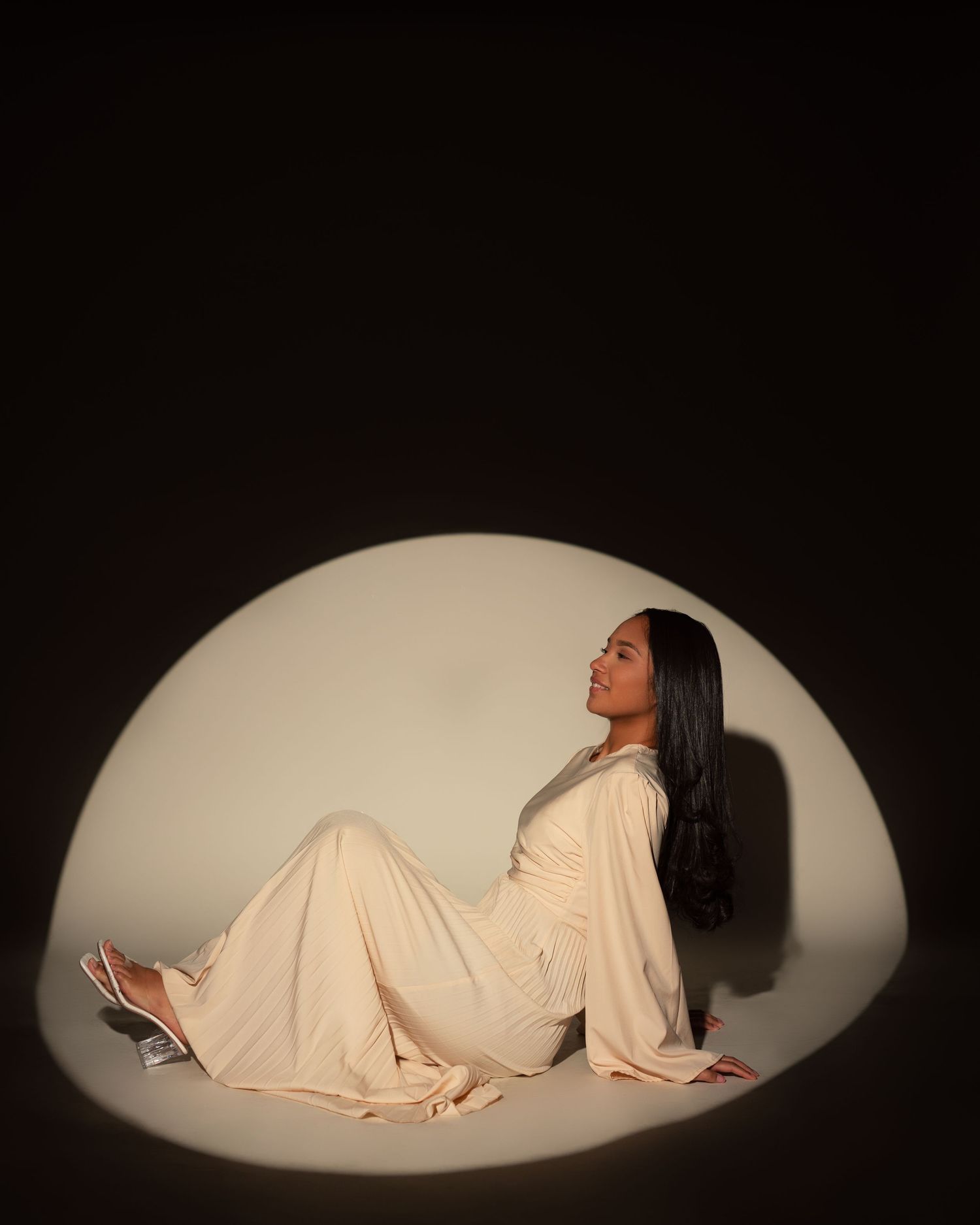 A progression of four dramatic poses in a spotlight showing a person in white lying down on a dark floor.