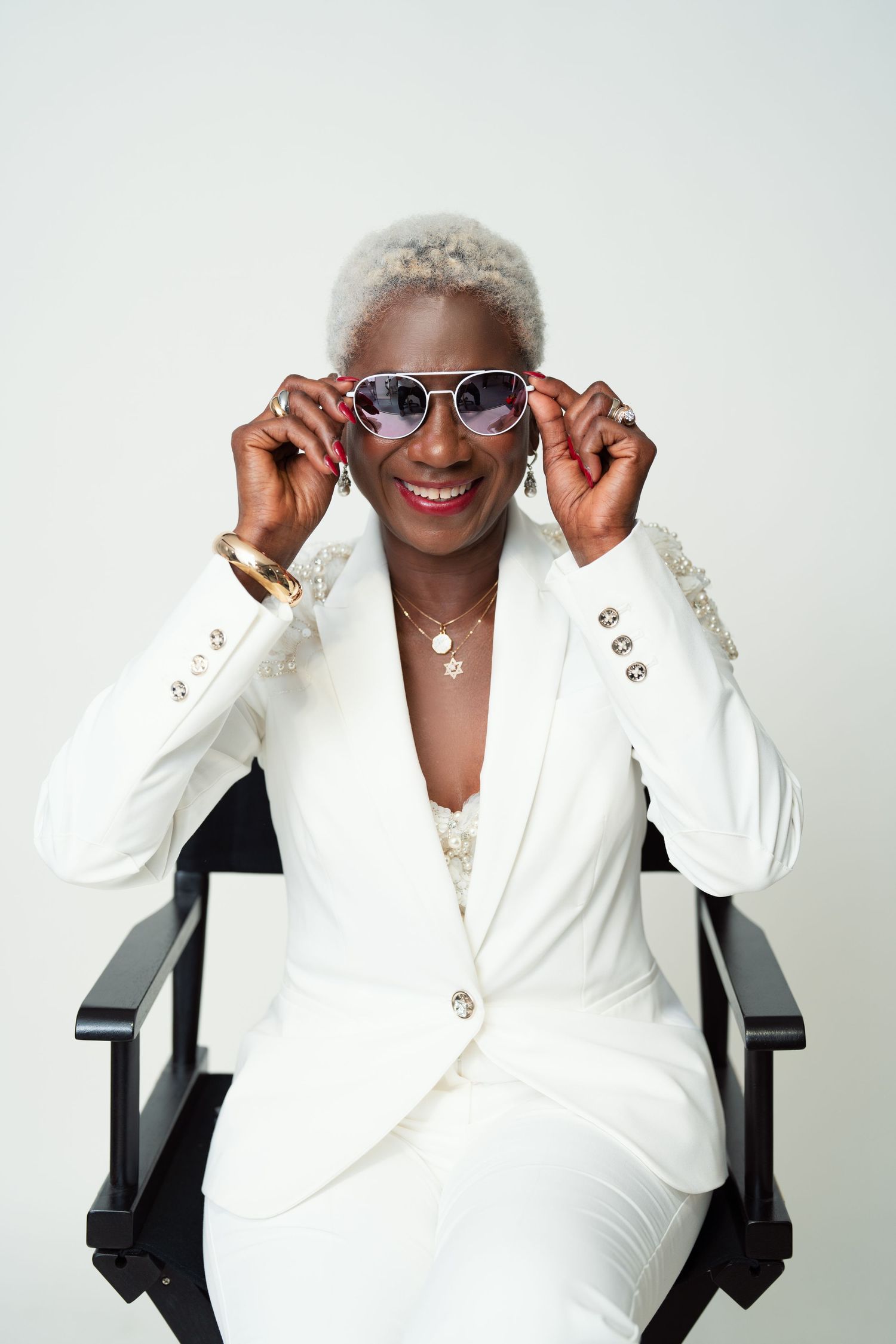 A cheerful person wearing a white blazer and sunglasses poses playfully in a sequence of three photos.