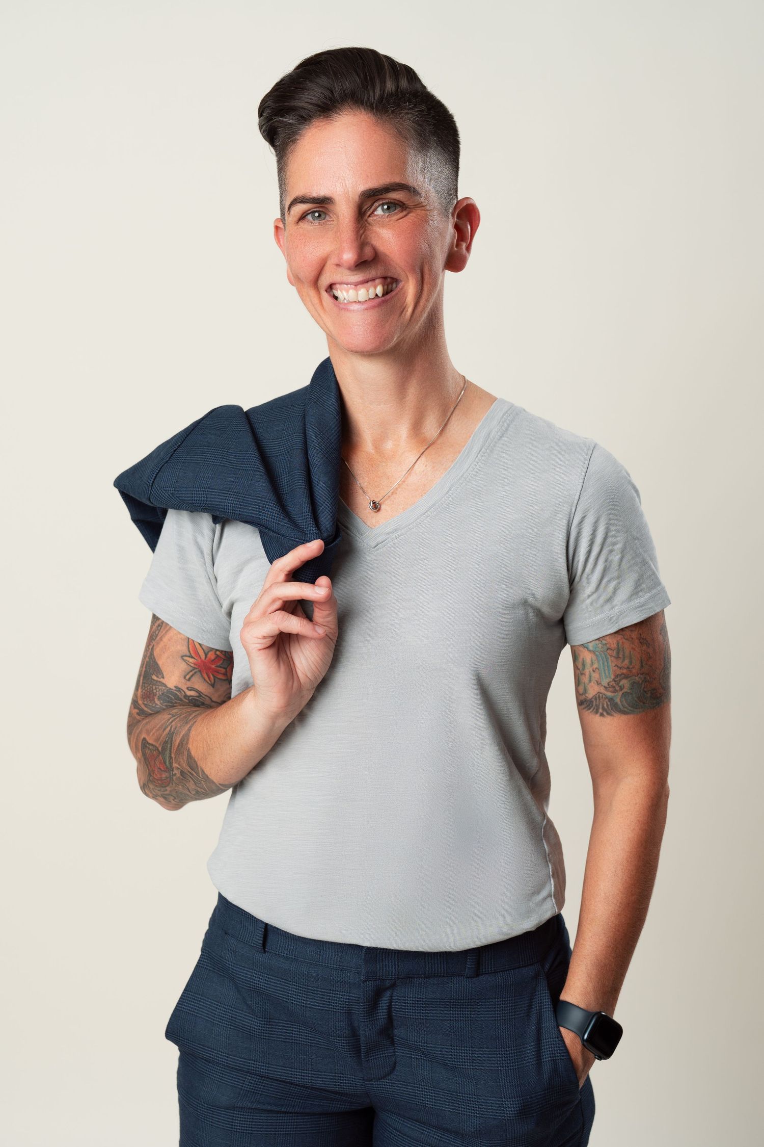 Casual styled person wearing a gray t-shirt and navy pants poses with arm gestures in a white studio setting.