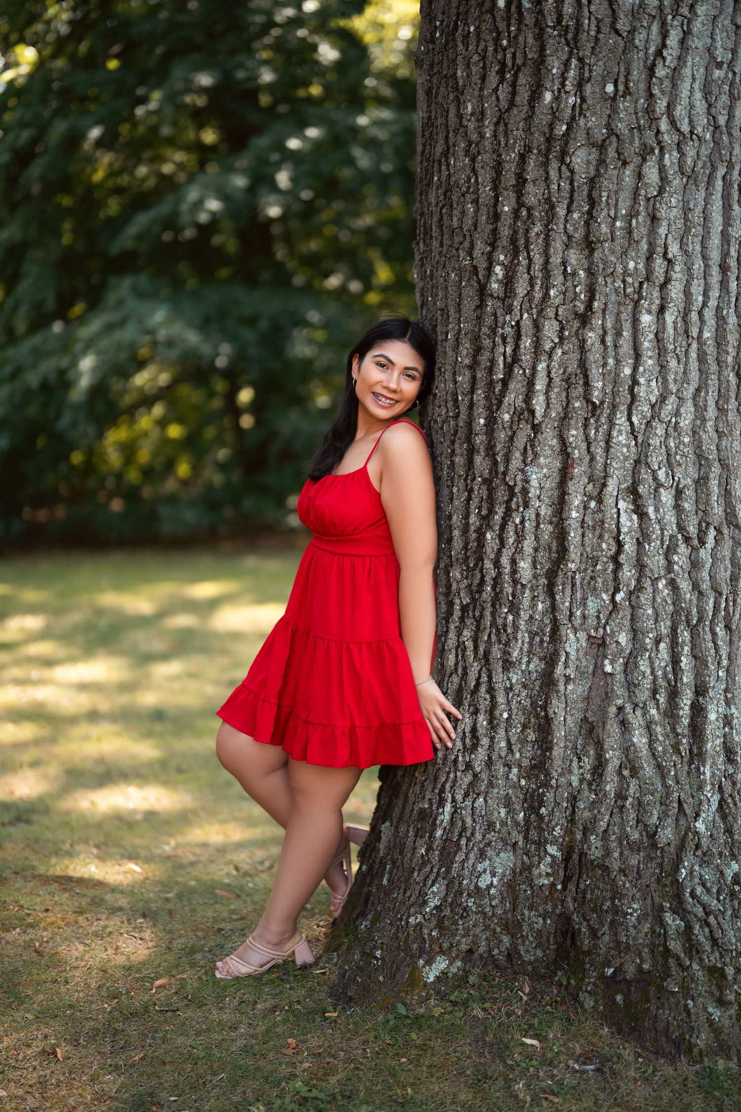 A series of four outdoor portraits in a red dress against large tree trunks with dappled sunlight filtering through leaves.