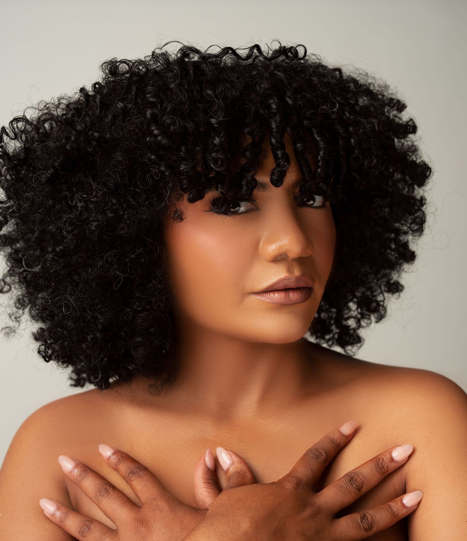Artistic beauty portrait showing close-up series of shoulders and curly natural hair against neutral background.