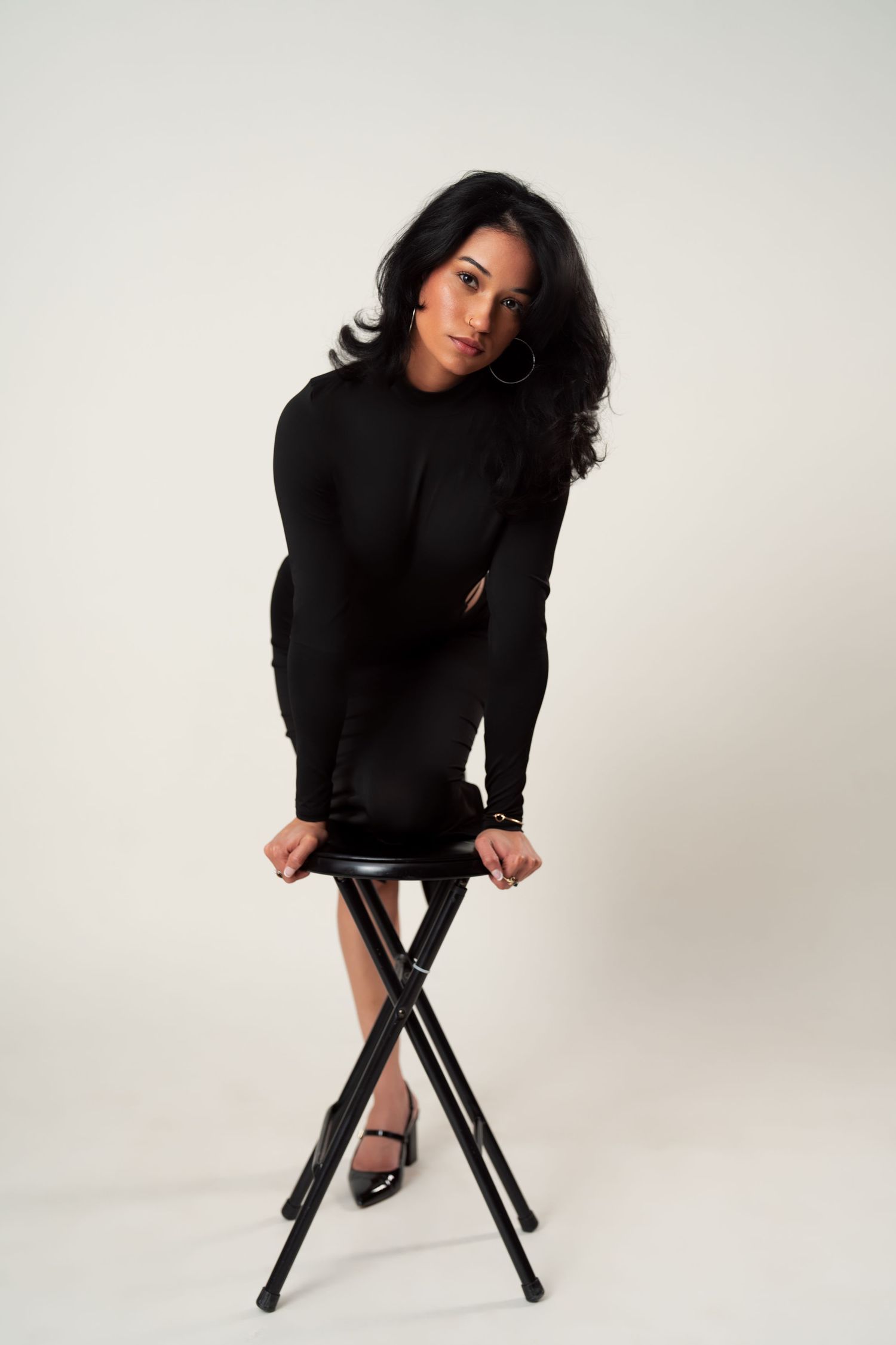 A model posing on a black stool against a white backdrop in various artistic poses wearing a black sweater.