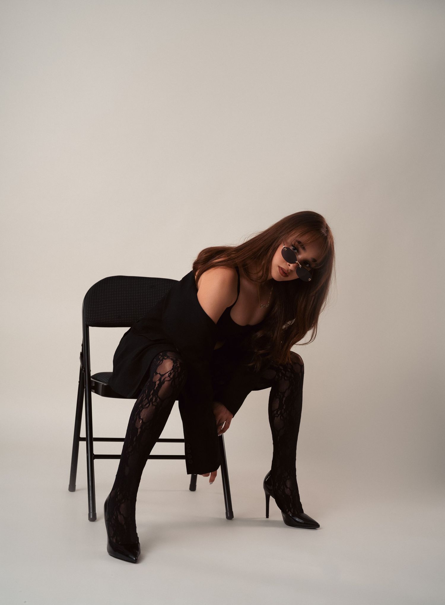 Professional photo series of someone posing dramatically on a black chair against a light gray studio backdrop.