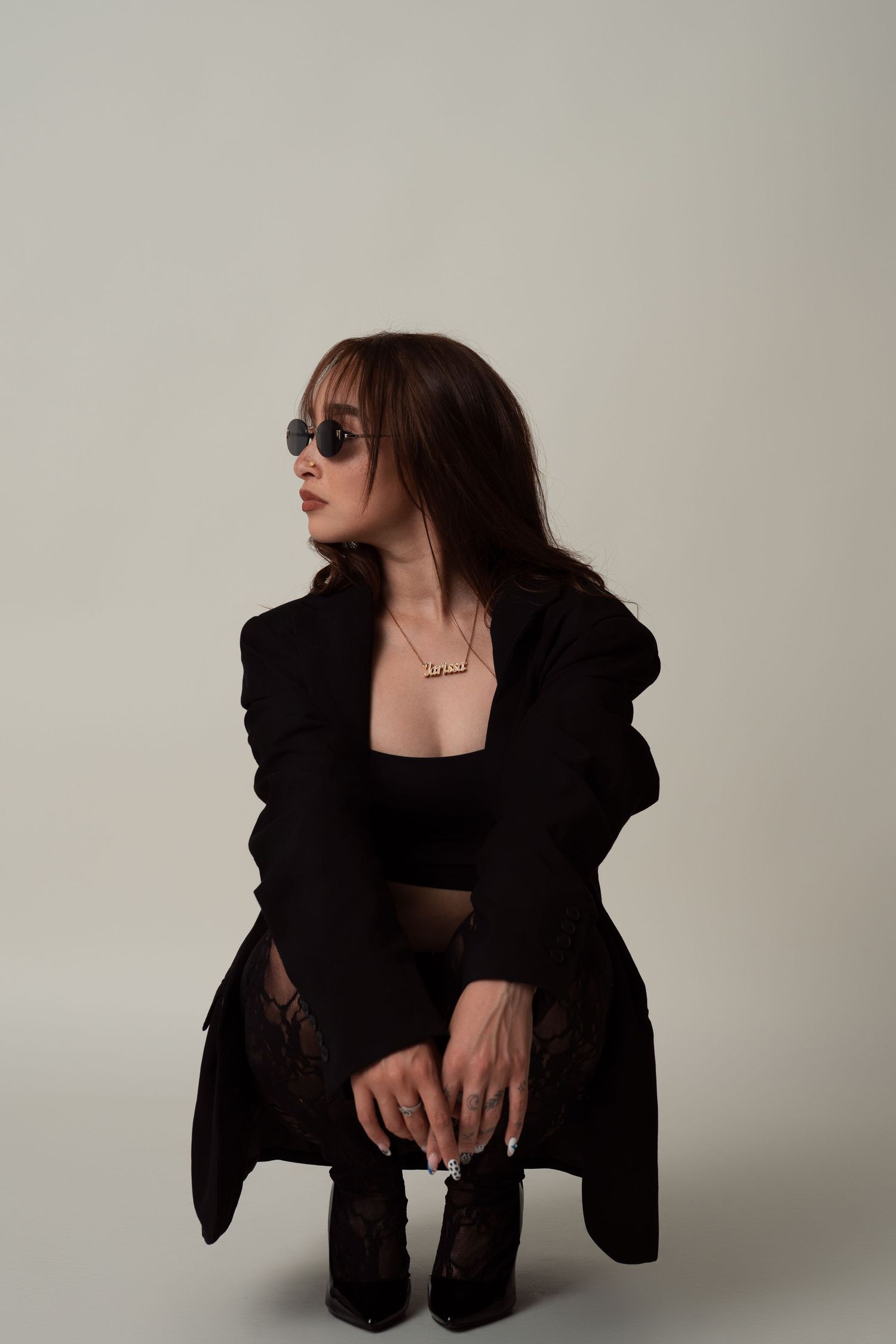 Fashion model in black outfit poses dramatically against neutral backdrop for artistic editorial photoshoot series.