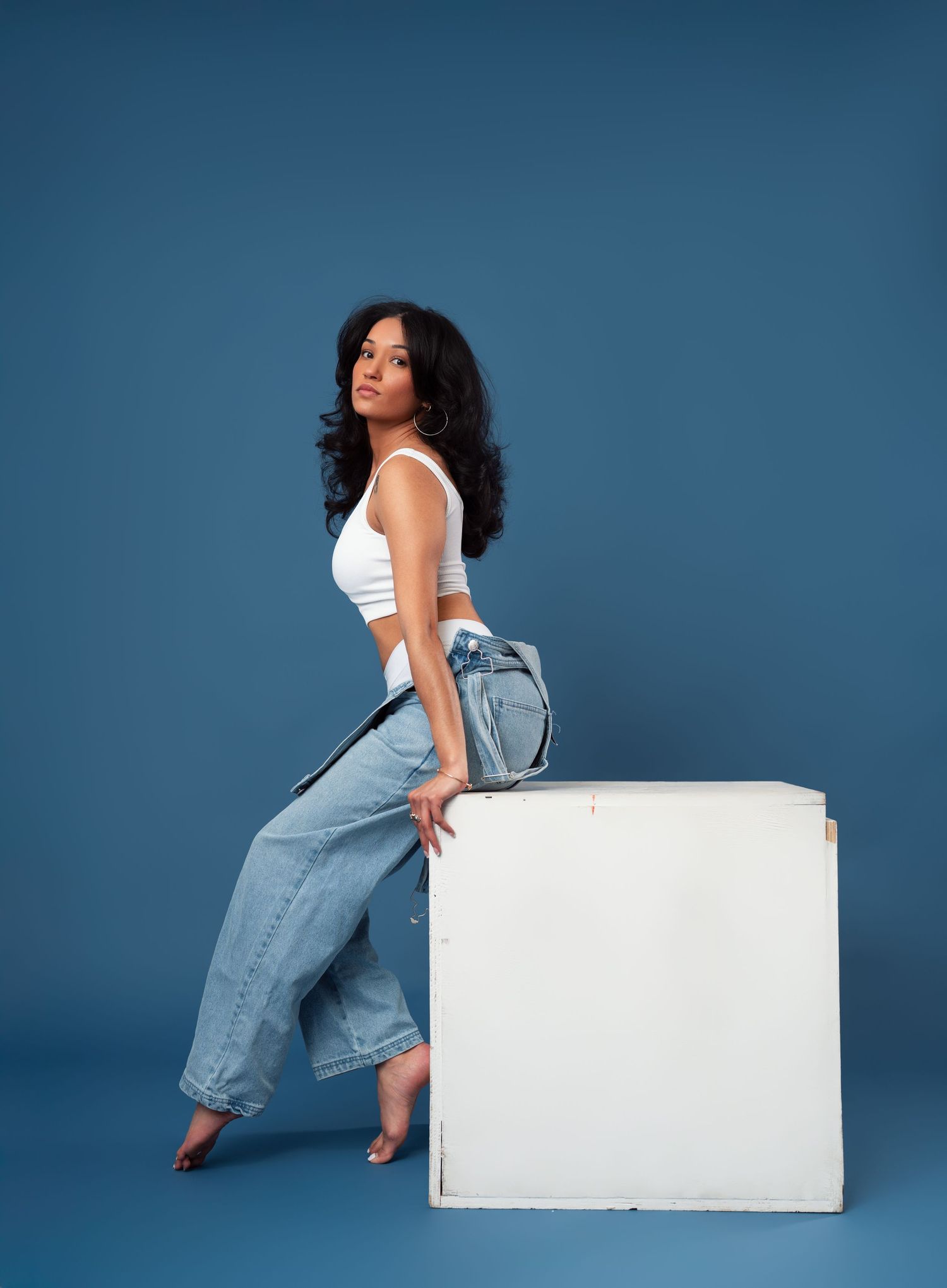 Figure striking artistic poses against blue wall while interacting with white rectangular prop in four-image series.
