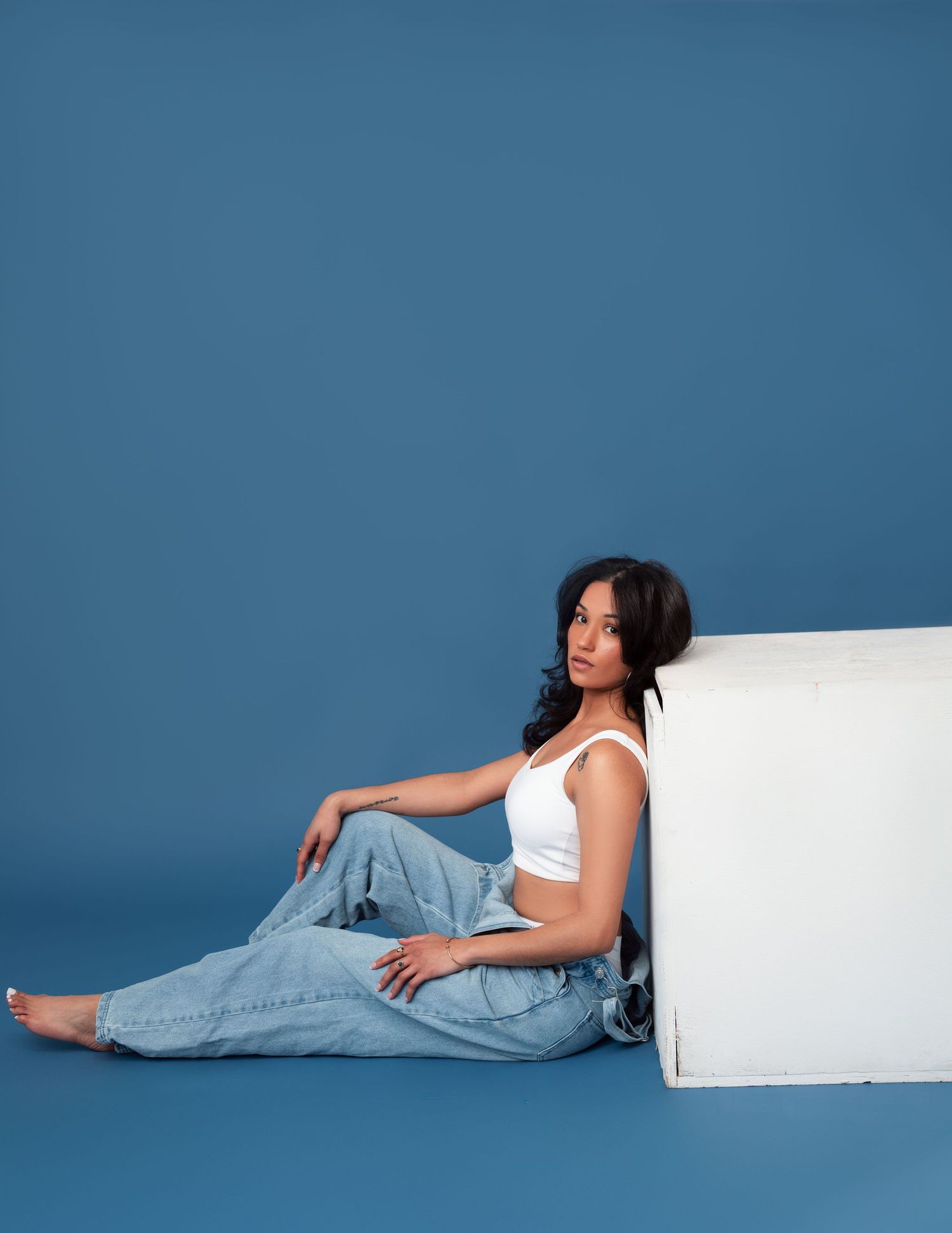 Artistic fashion photo series against blue backdrop showing person in casual denim and white top in lounging poses.