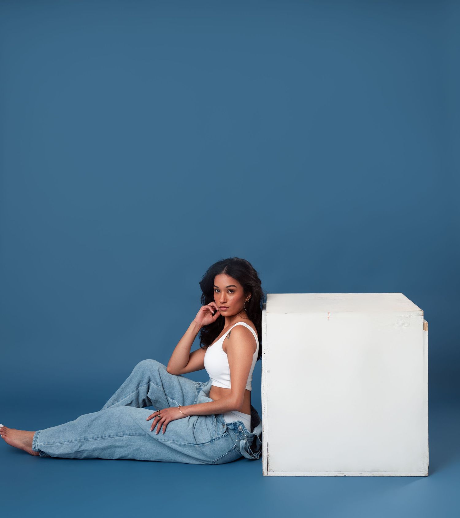Person in casual attire reclines against white blocks in an artistic portrait series with blue background.