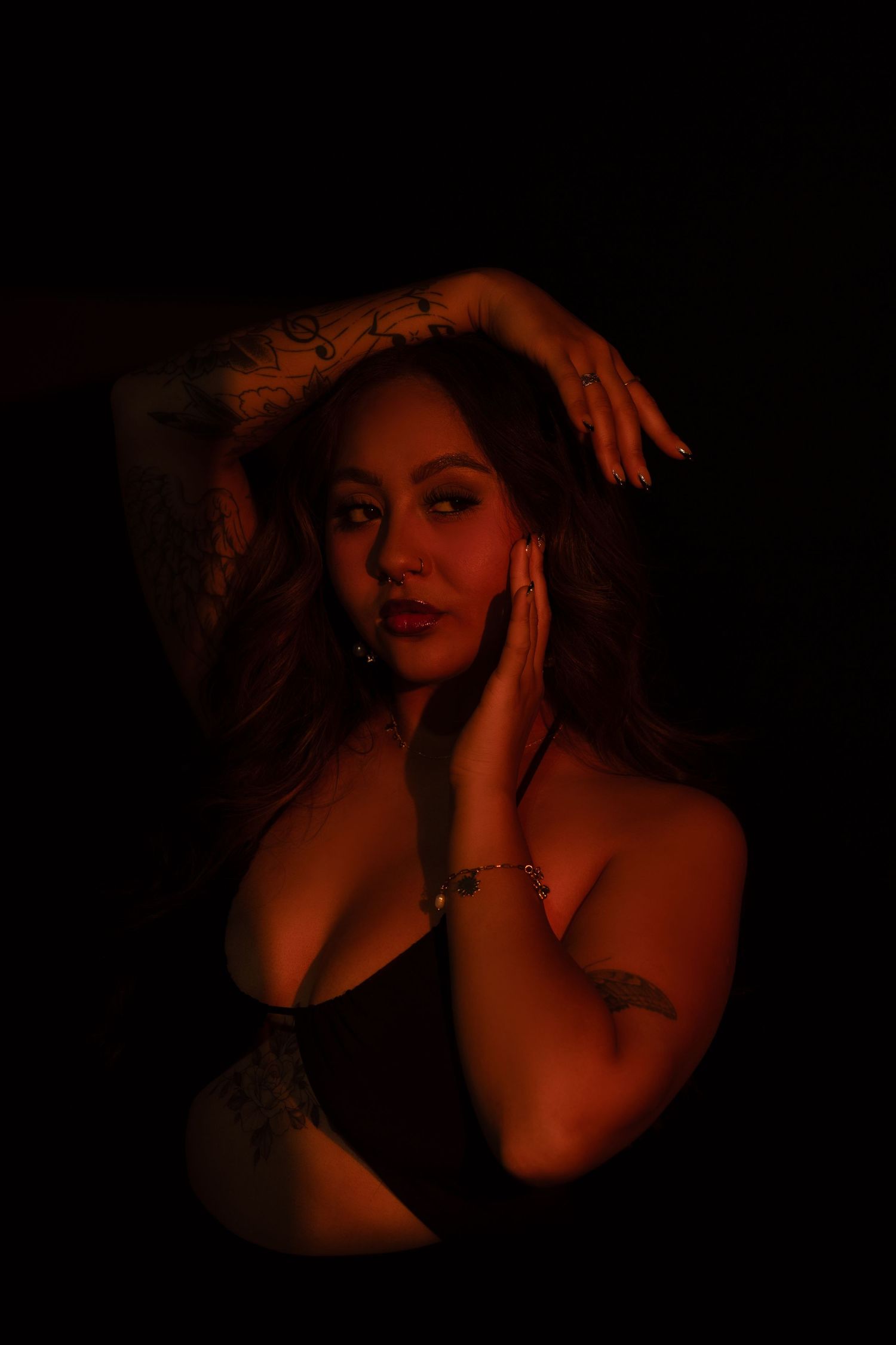 Woman with dark ginger hair poses in moody boudoir photoshoot with dramatic orange lighting.