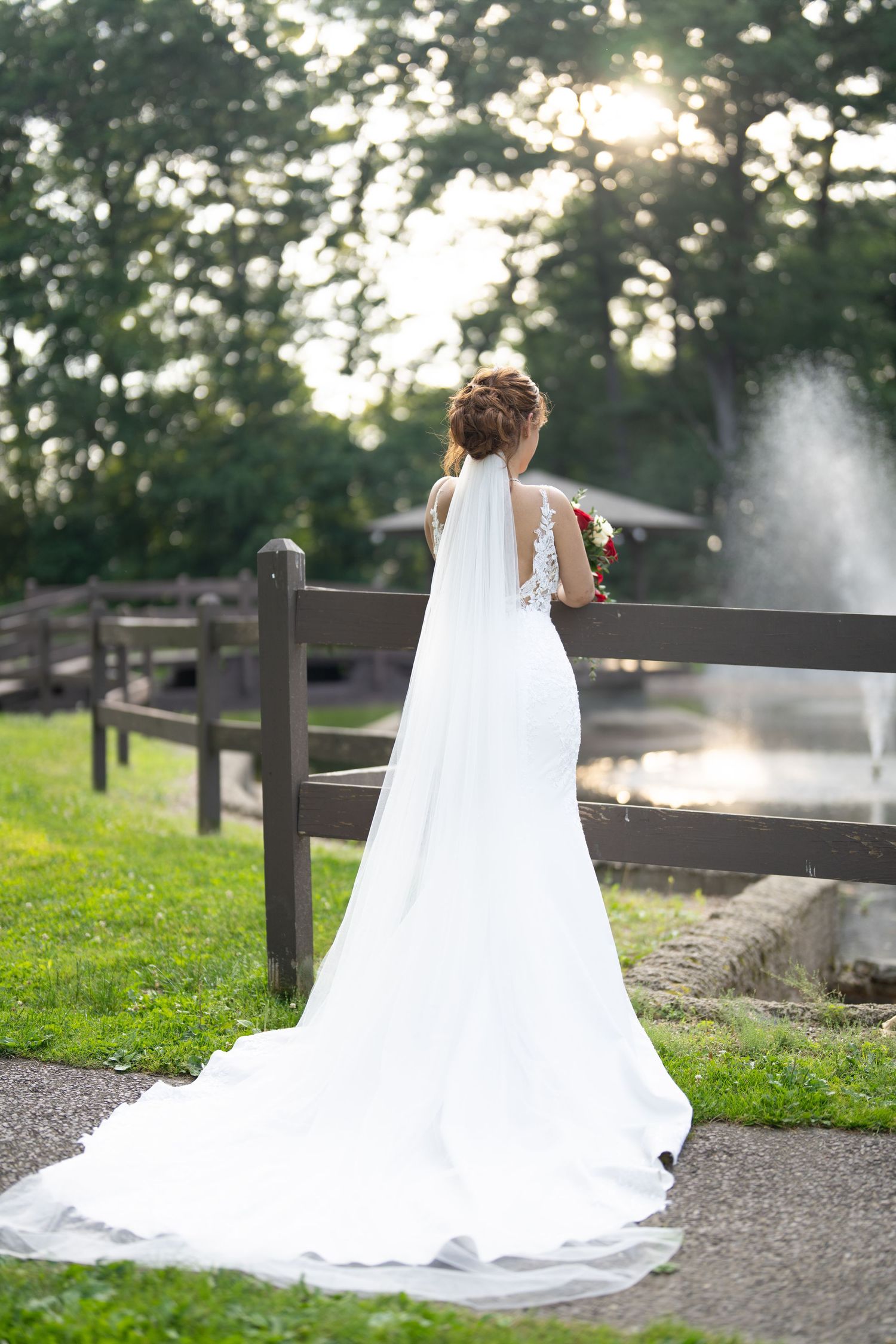 Flowing white wedding gown with long cathedral train photographed from behind in an evening garden setting.