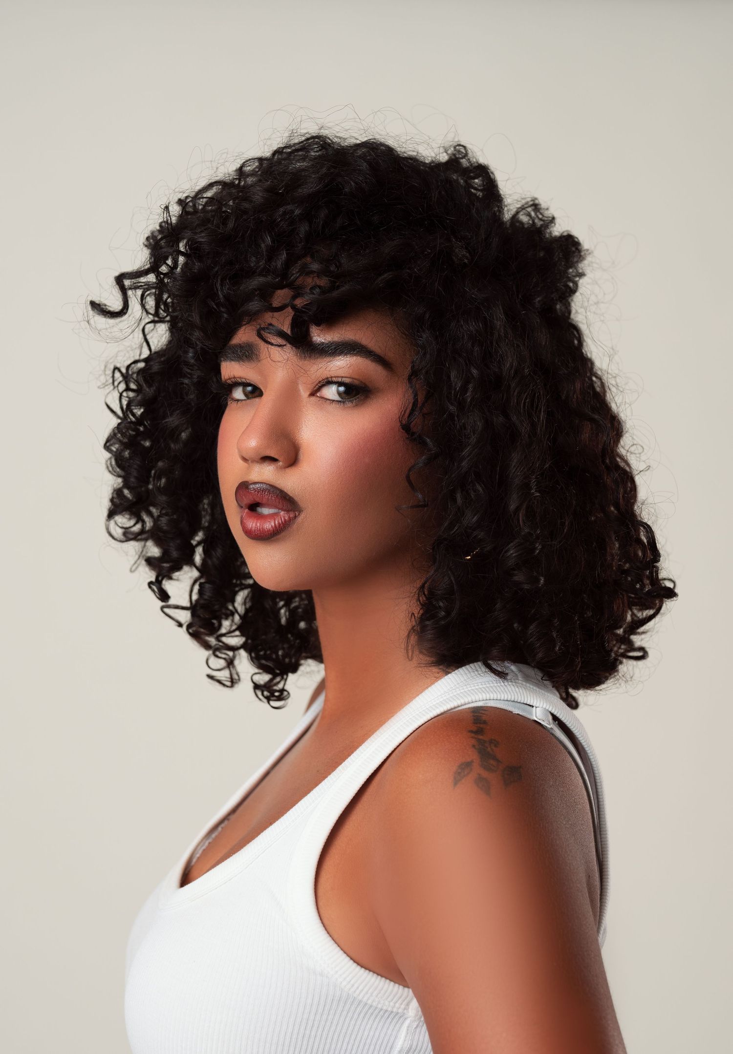 Fashion portrait series showing a curvy model with natural curly hair wearing a white tank top against a light background.