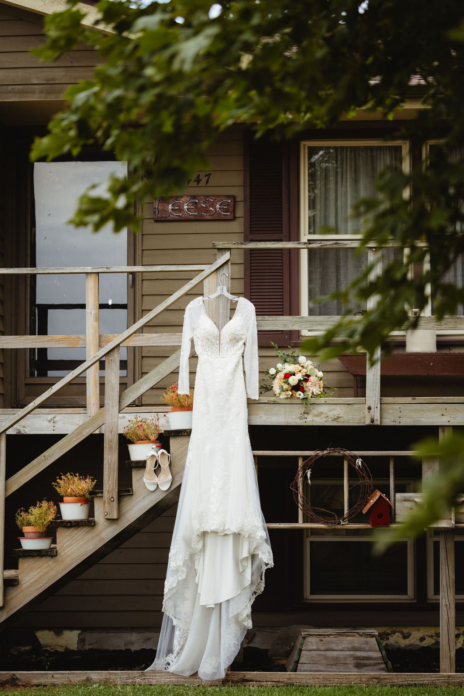 White wedding dress and accessories displayed on a rustic wooden porch railing with potted plants.