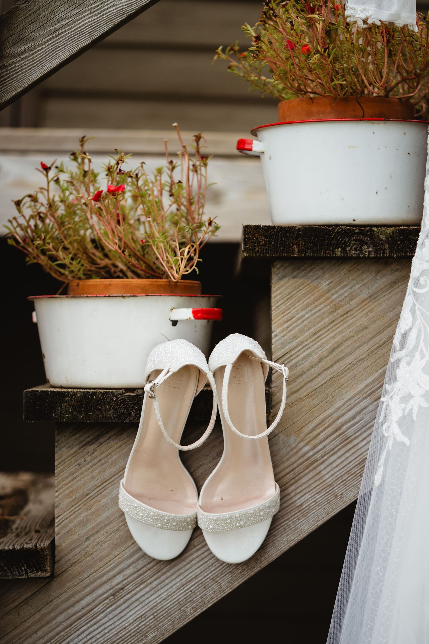 Elegant white bridal shoes arranged on weathered wooden deck steps with terracotta planters.