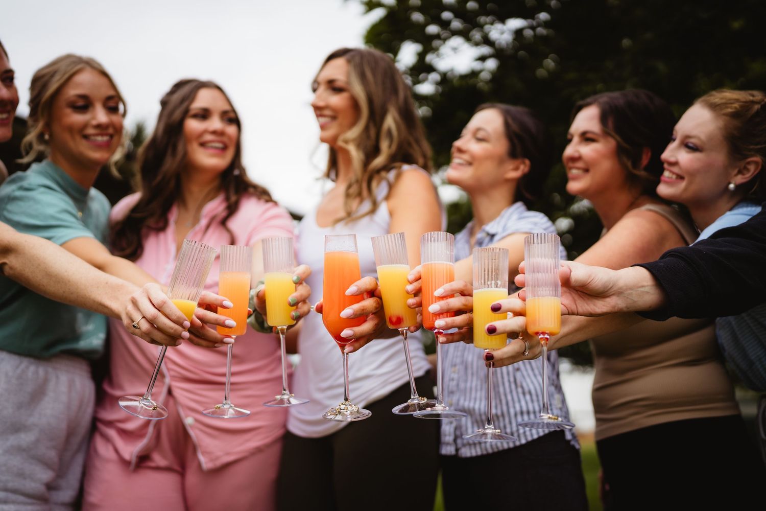 Friends gather outdoors toasting and clinking colorful cocktail glasses while laughing and chatting together.