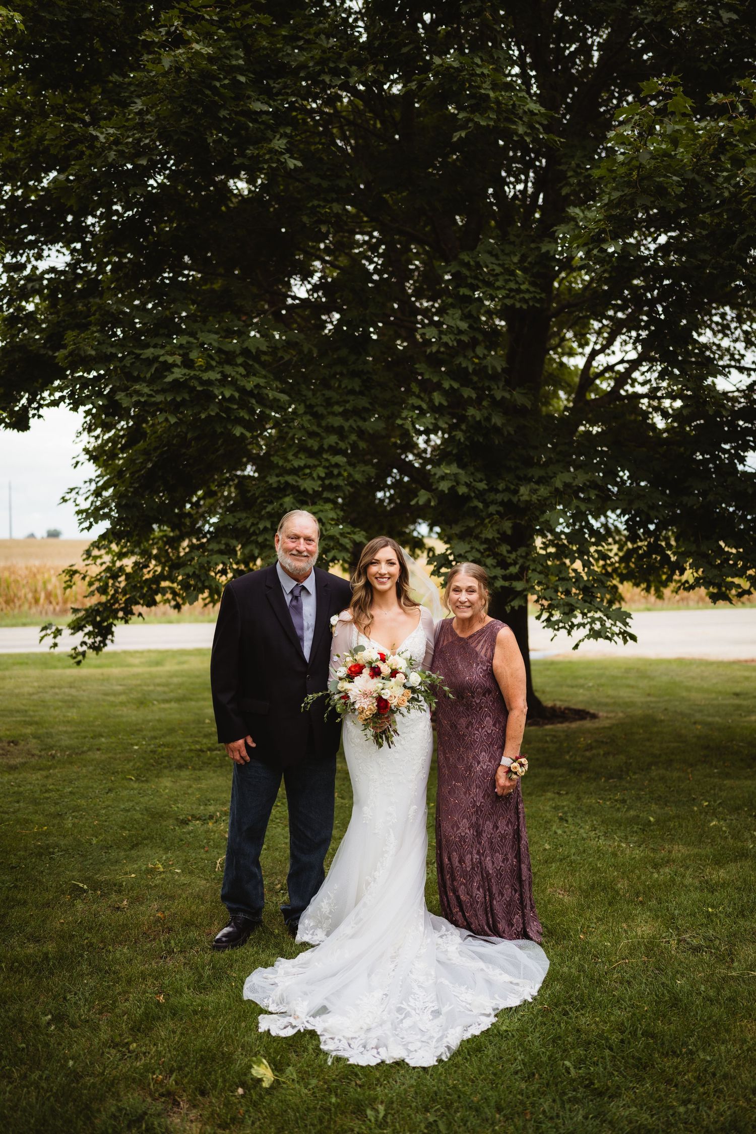 Four outdoor wedding photos show a group in burgundy and formal attire posing together under trees in a grassy field.