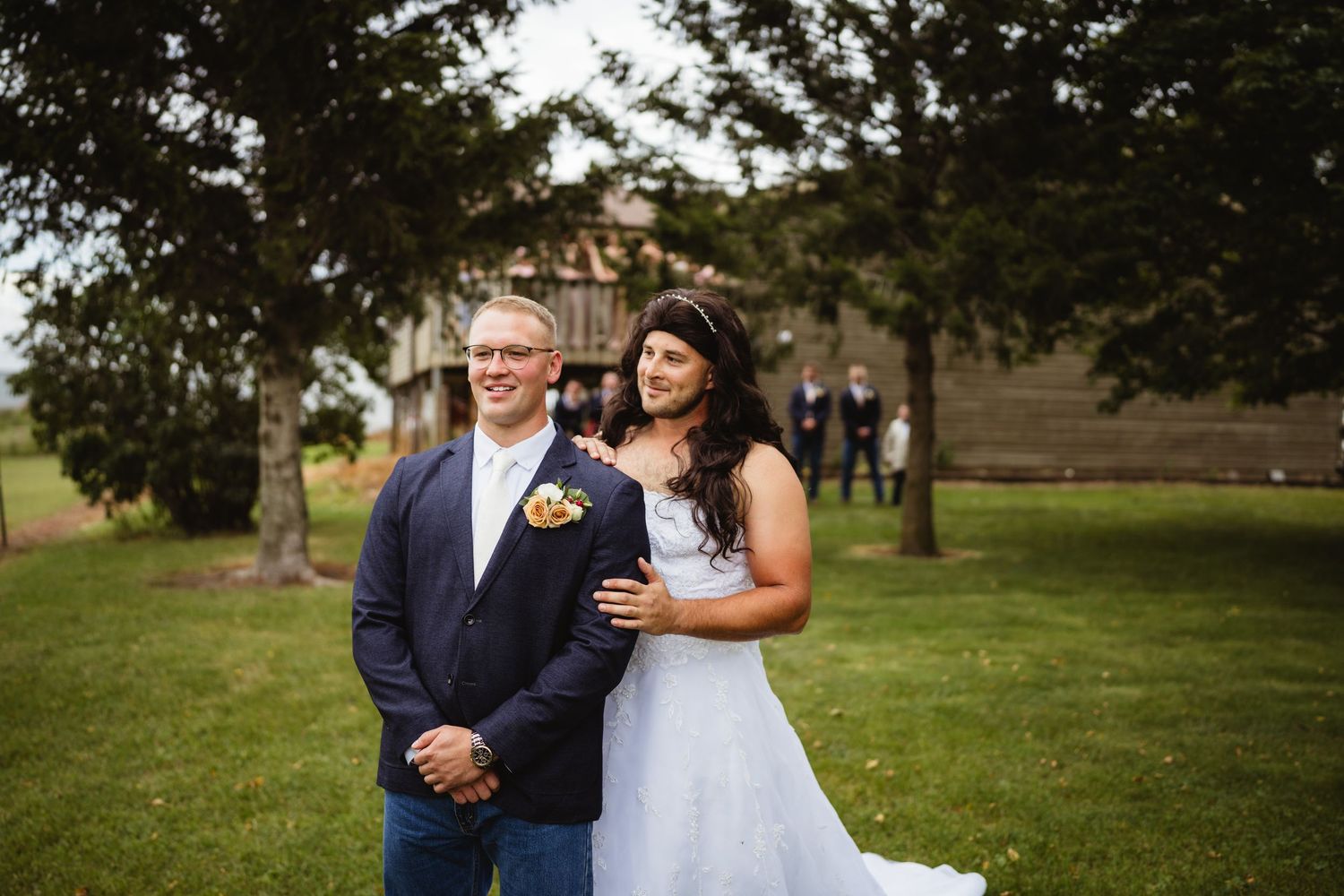 A couple embraces during an outdoor wedding photoshoot while standing in a grassy field.
