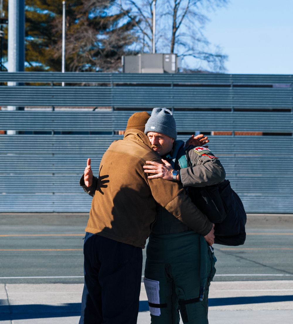 Two people embracing outdoors in front of empty stadium bleachers.