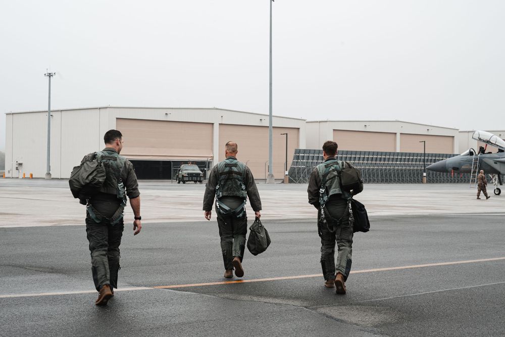 Three military personnel walking across airfield carrying gear bags.