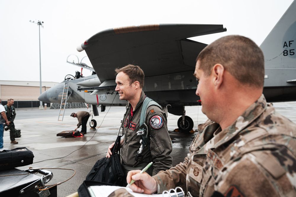 Military personnel reviewing documents near aircraft on airfield tarmac.