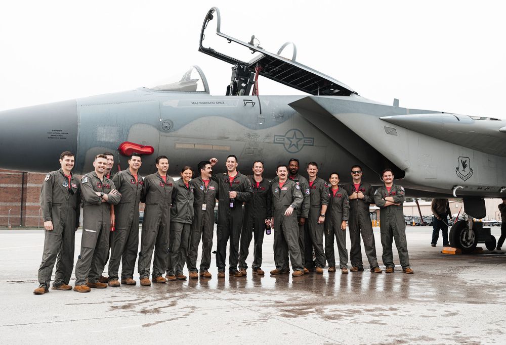 Military crew lined up in formation beside an aircraft on the runway.