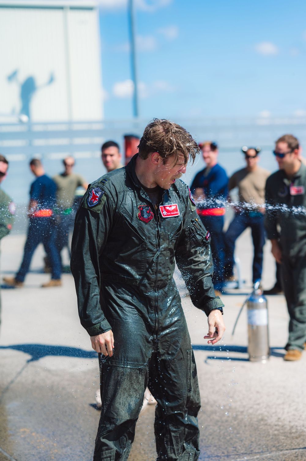 Military pilot in flight suit gets sprayed with water in traditional aviation ceremony.