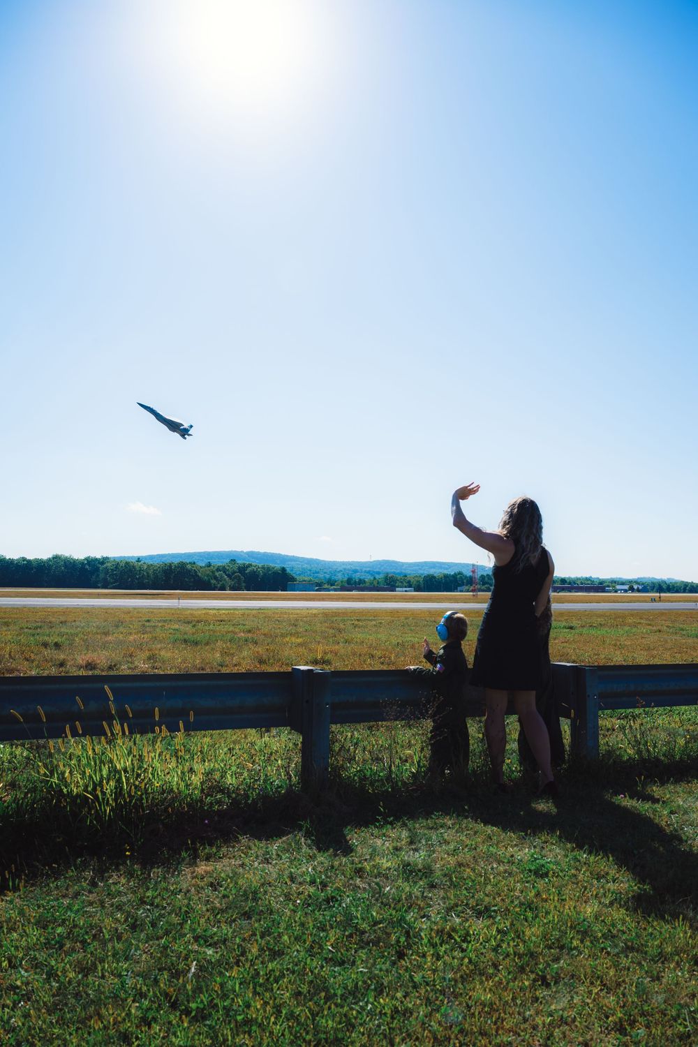 Silhouette of person and dog watching airplane take off against bright blue sky.