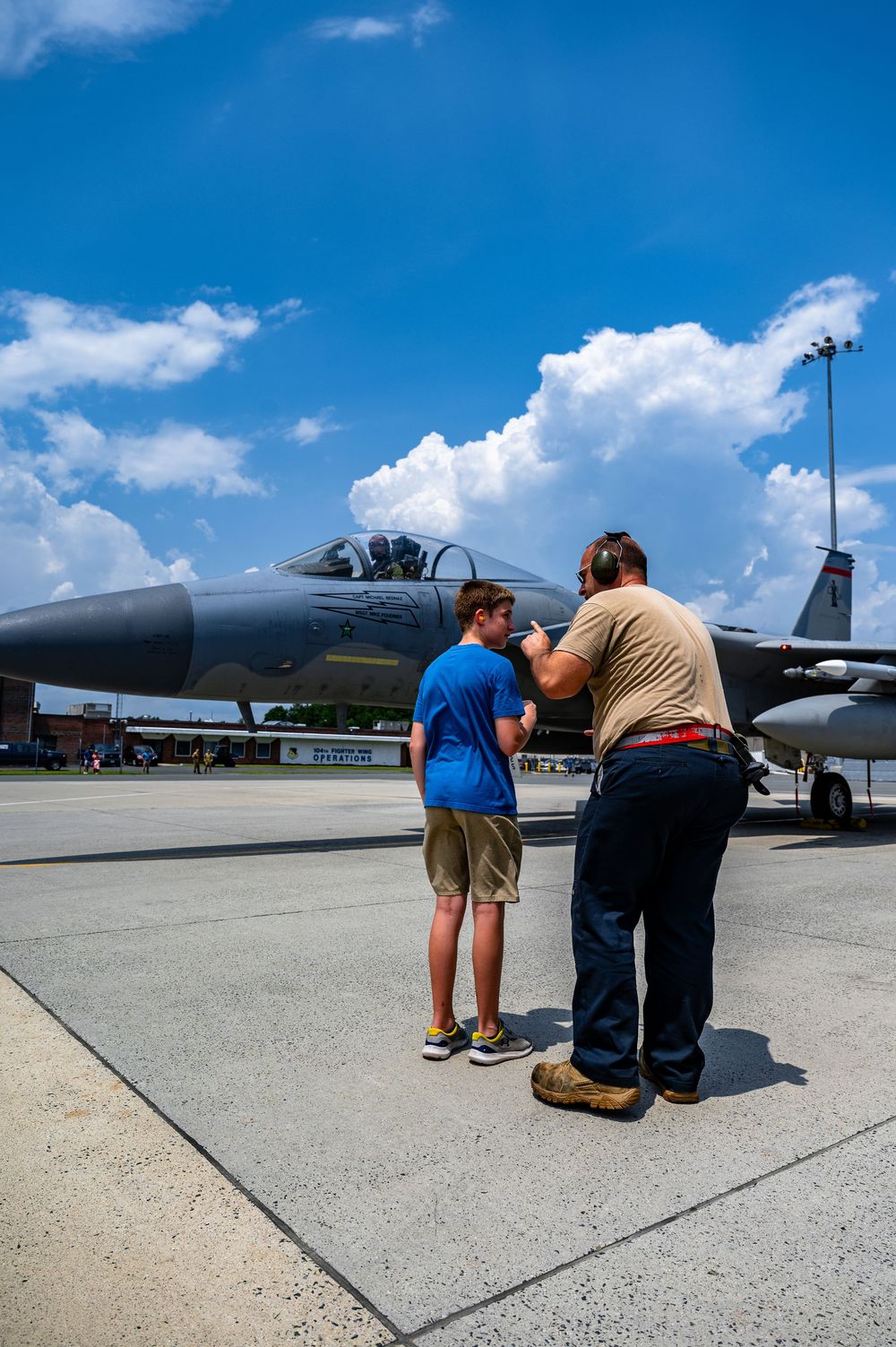 Personnel inspecting the underside of a military aircraft on a sunny day.