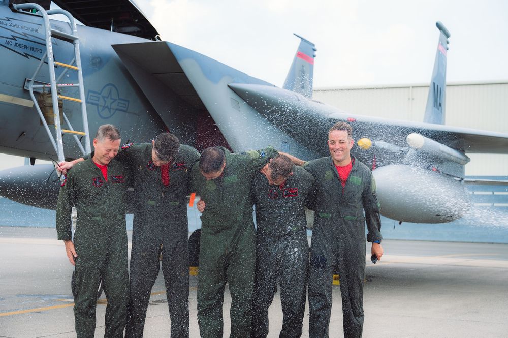 Group of military members getting sprayed with water in an aircraft celebration tradition.