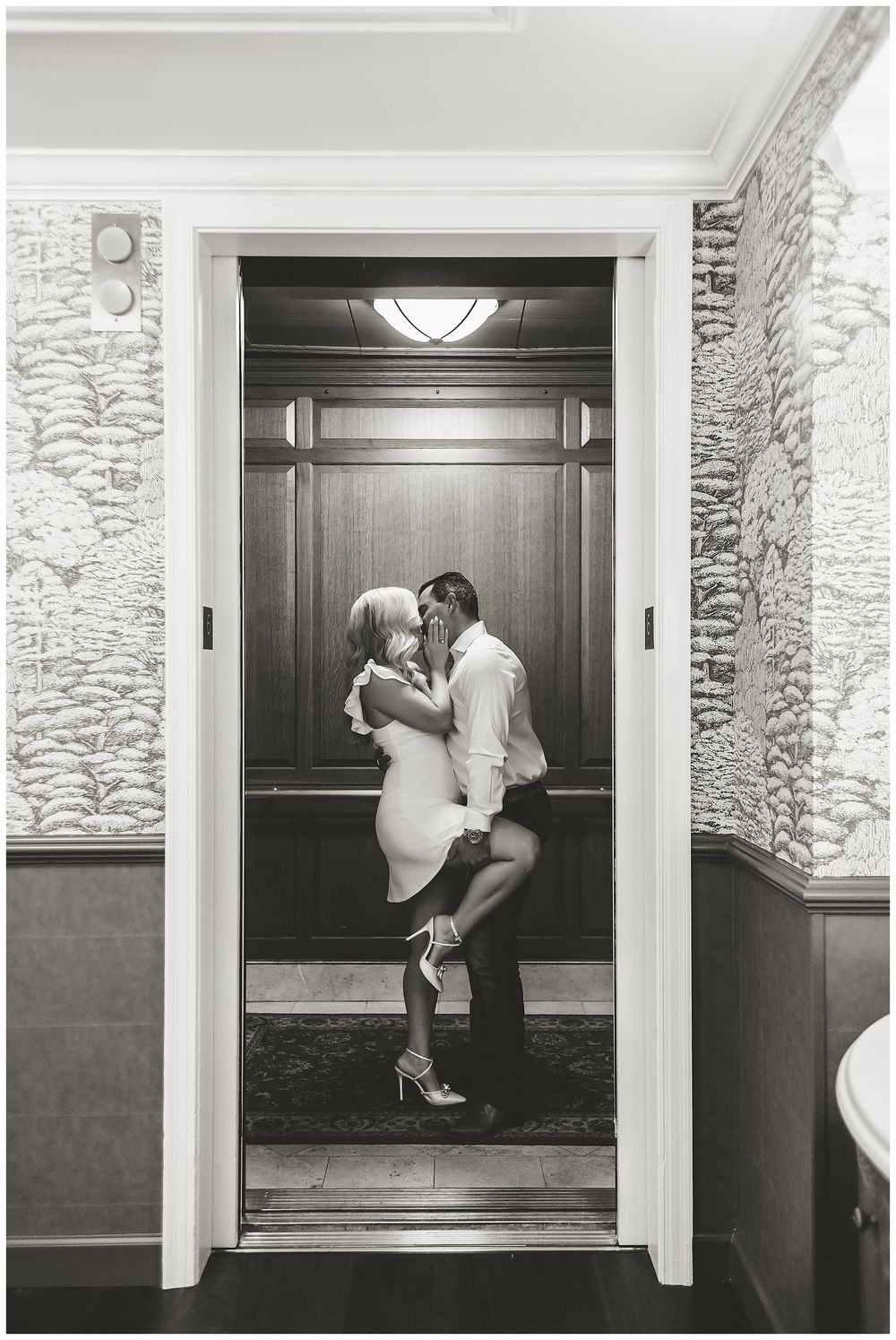 A romantic black and white photograph of a couple embracing in an elevator with elegant interior details.