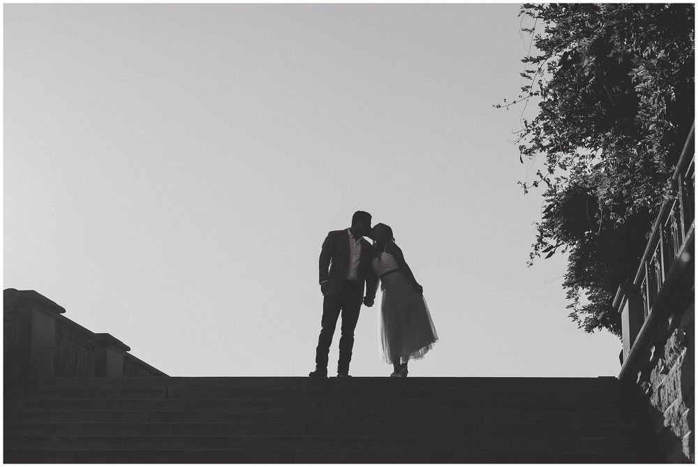 A silhouetted couple stands together against a bright sky in a romantic black and white photograph.