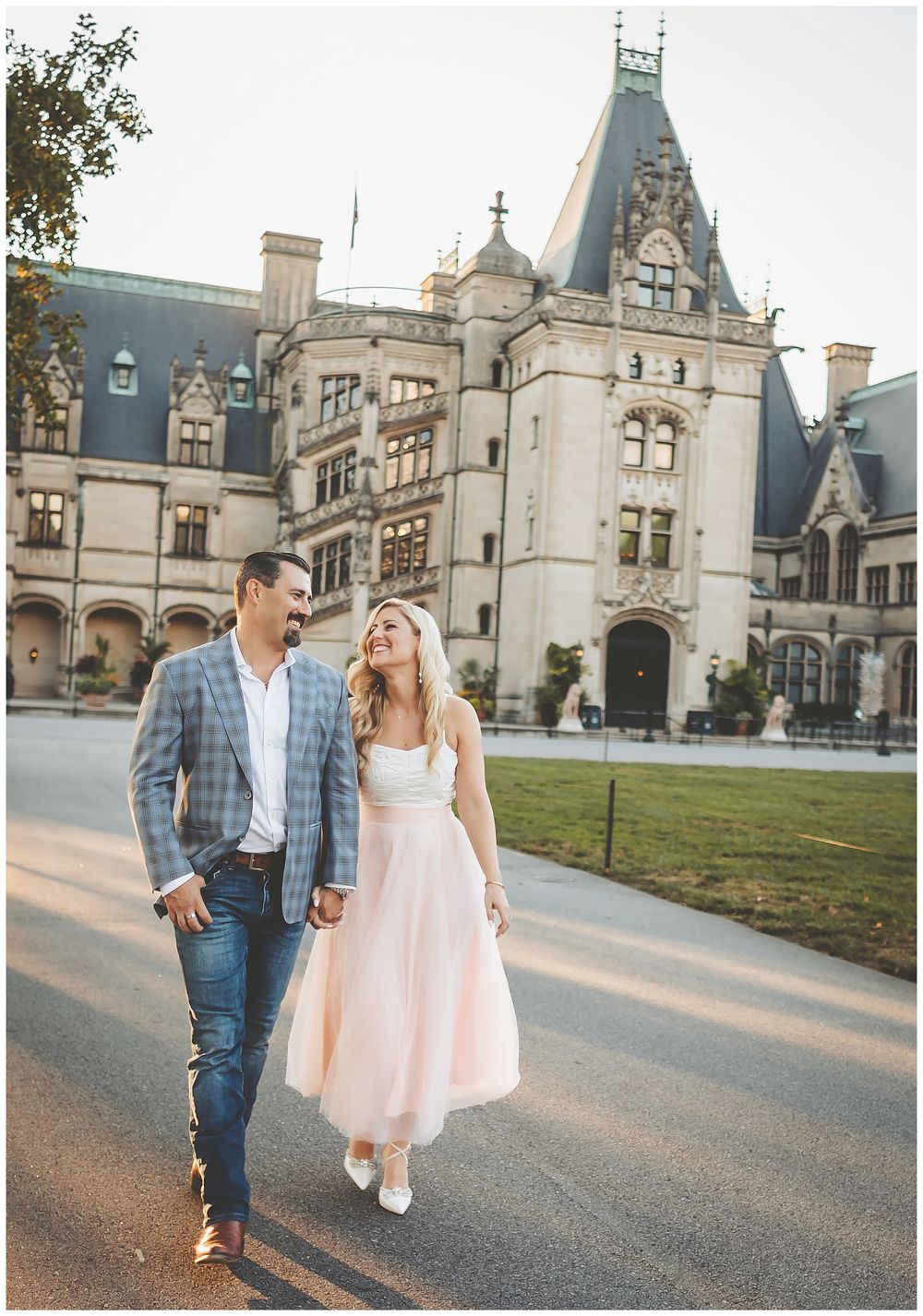 A romantic couple in formal attire poses for photos at a grand stone mansion with Gothic architecture details.