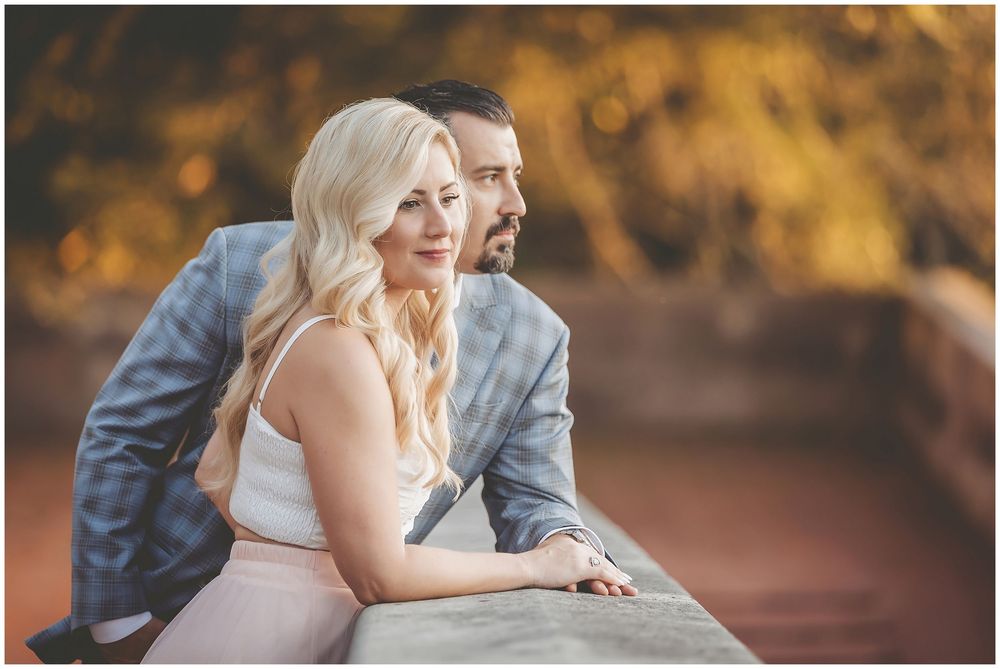Couple in formal attire sharing romantic moments during an outdoor autumn photoshoot with golden lighting.
