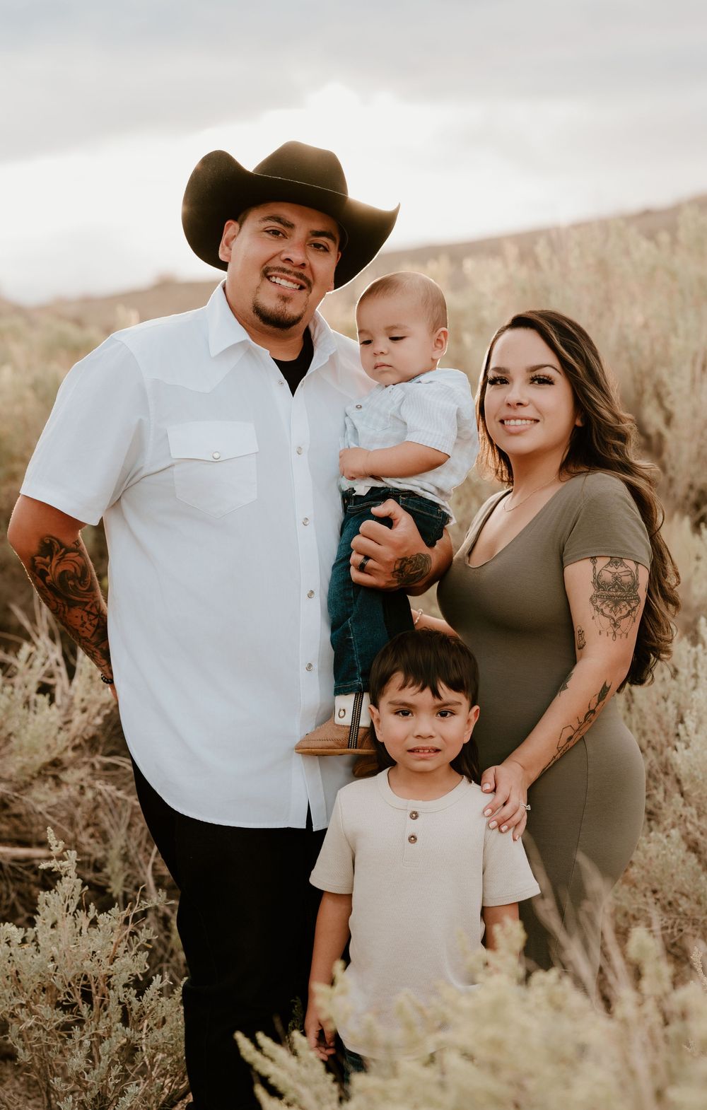A family in western attire poses together in a desert landscape during golden hour for a casual outdoor photoshoot.