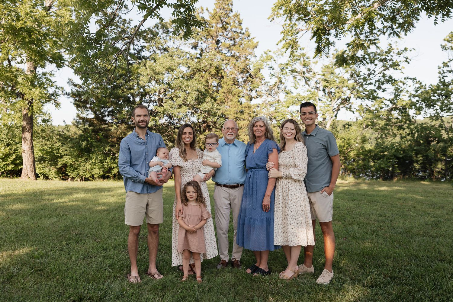 extended family standing in front of tree line smiling at camera at lake olathe Family photographers kansas city