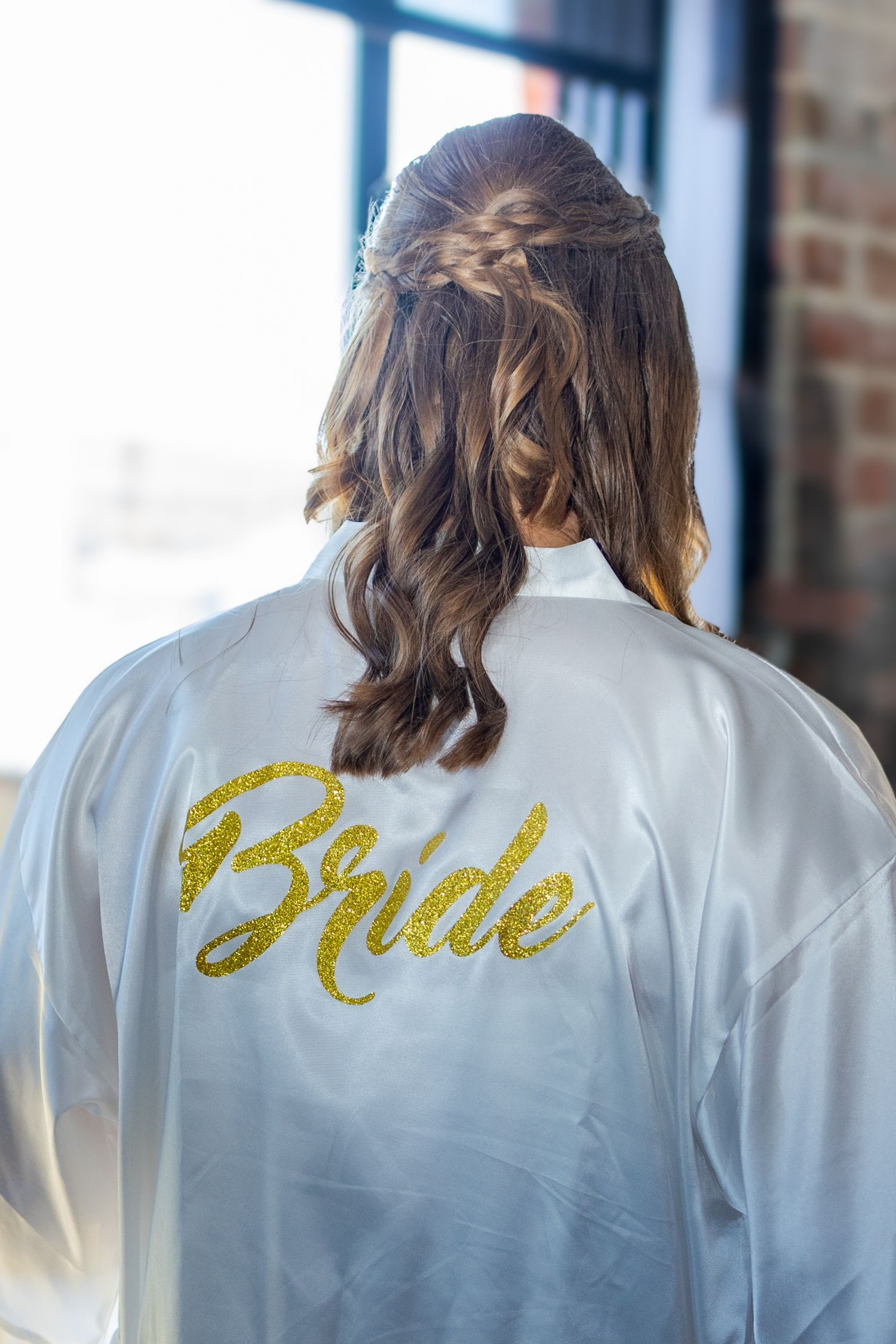 A white satin robe with 'Bride' written in gold glitter text on the back.