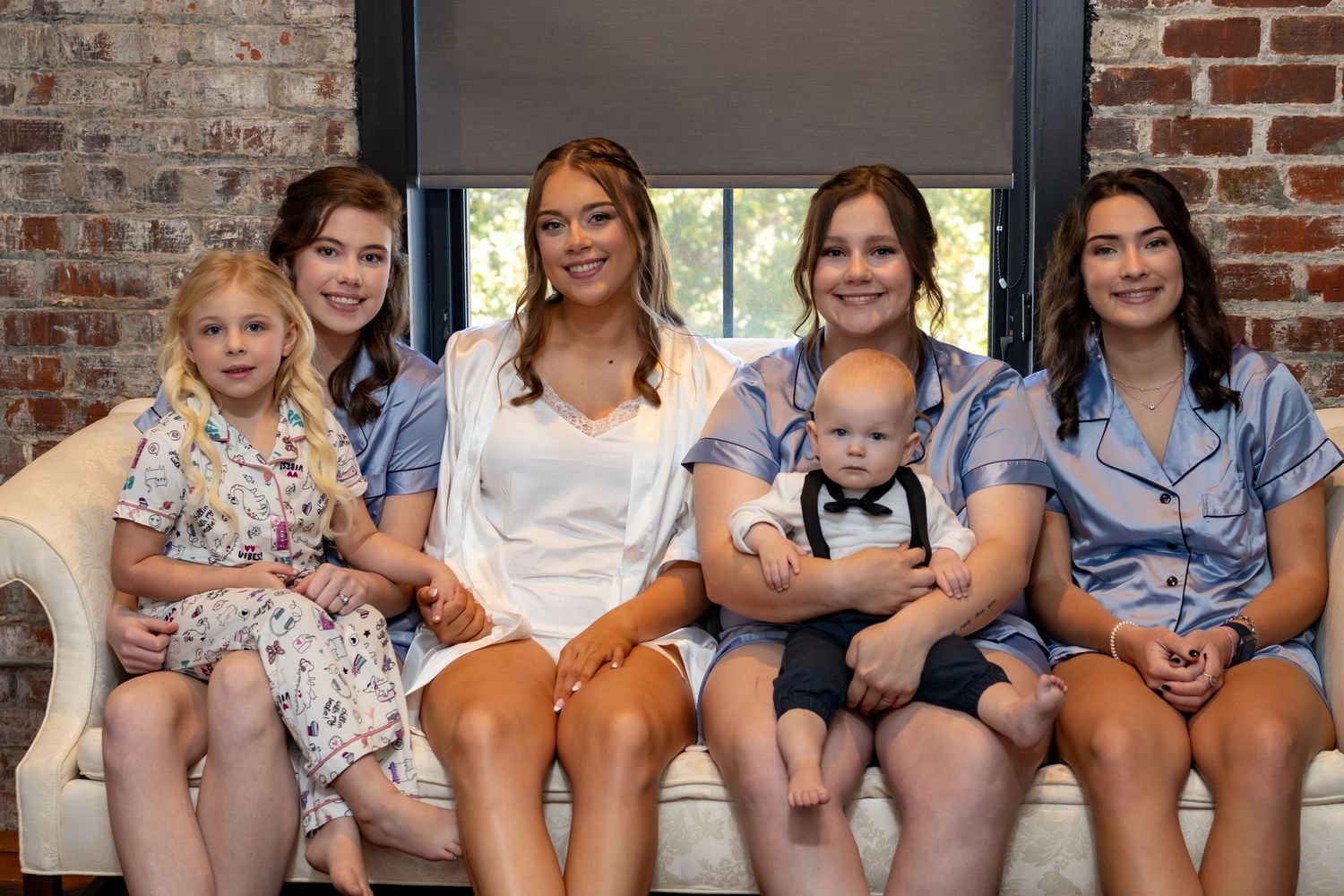 A group of children and adults sit together on a couch in a room with exposed brick walls.