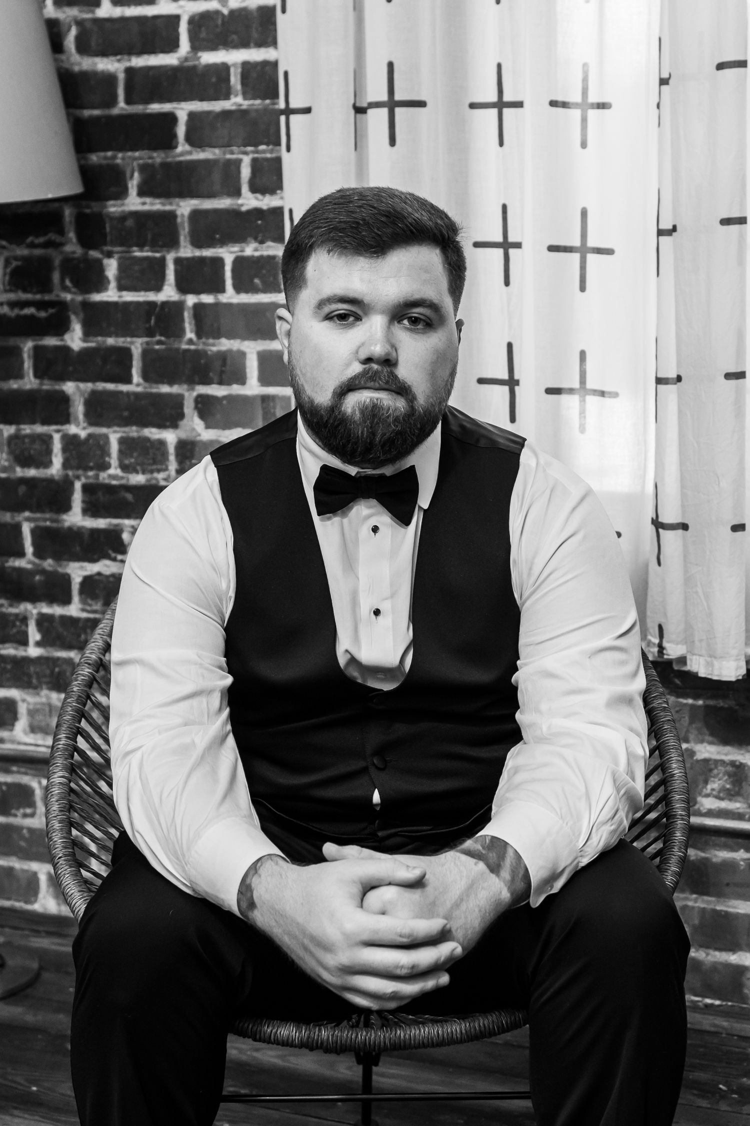A man in formal attire sits reflectively on steps against a brick wall background.