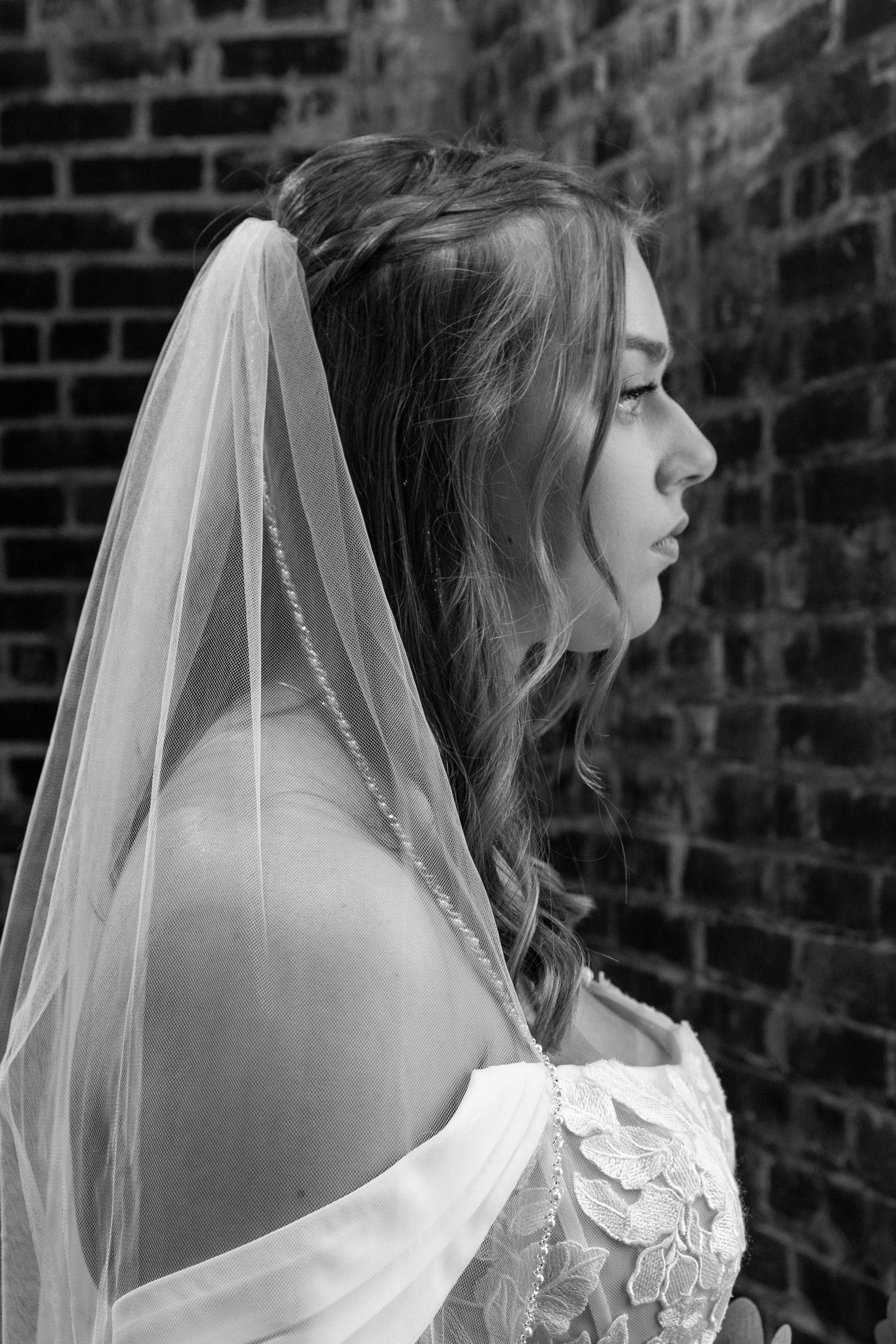 A bridal portrait photo session against an exposed brick wall showing the back details of a lace wedding gown with veil.