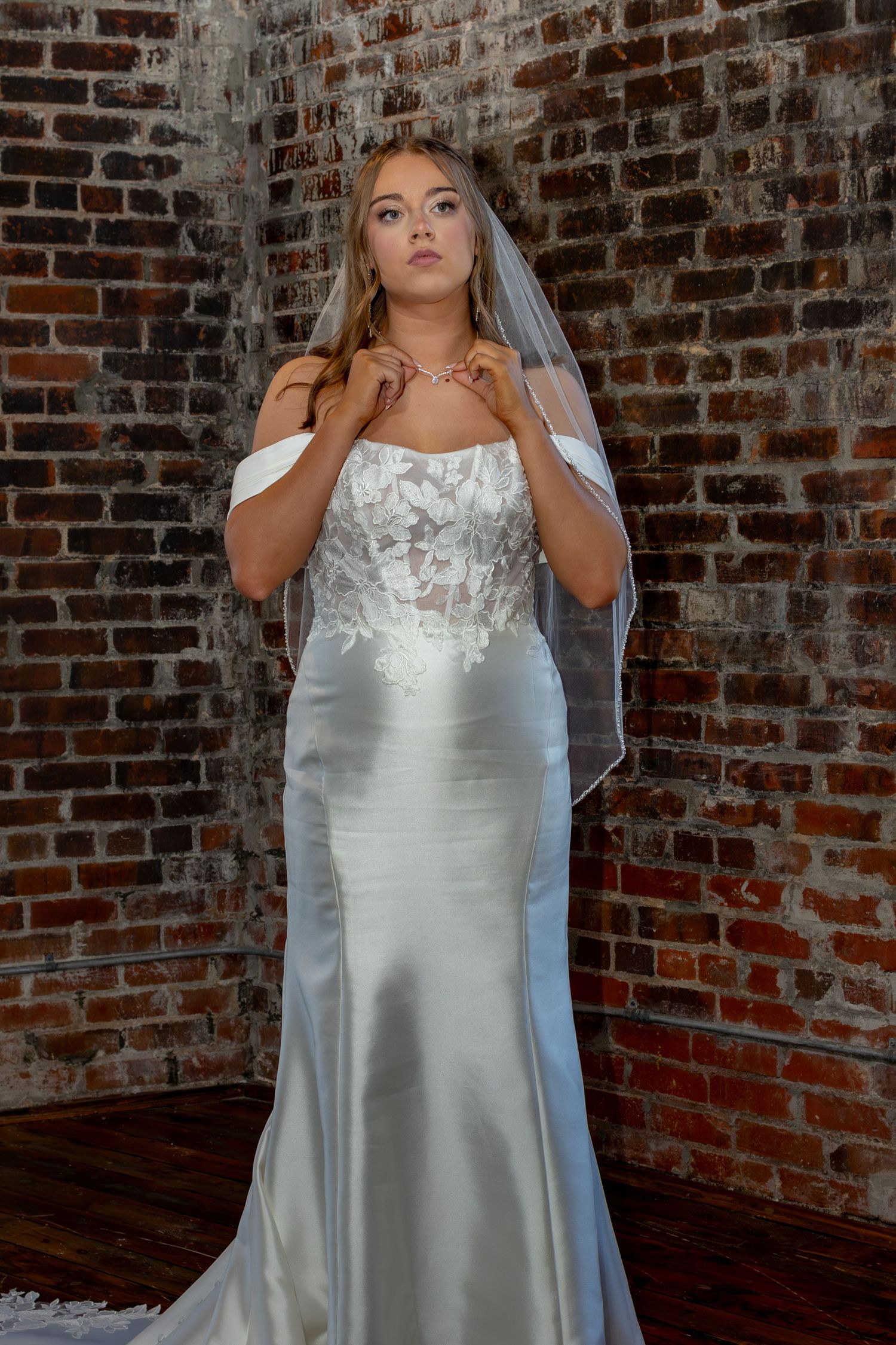 Wedding dress detail shot displaying intricate white lace bodice and sheer veil against rustic brick backdrop.