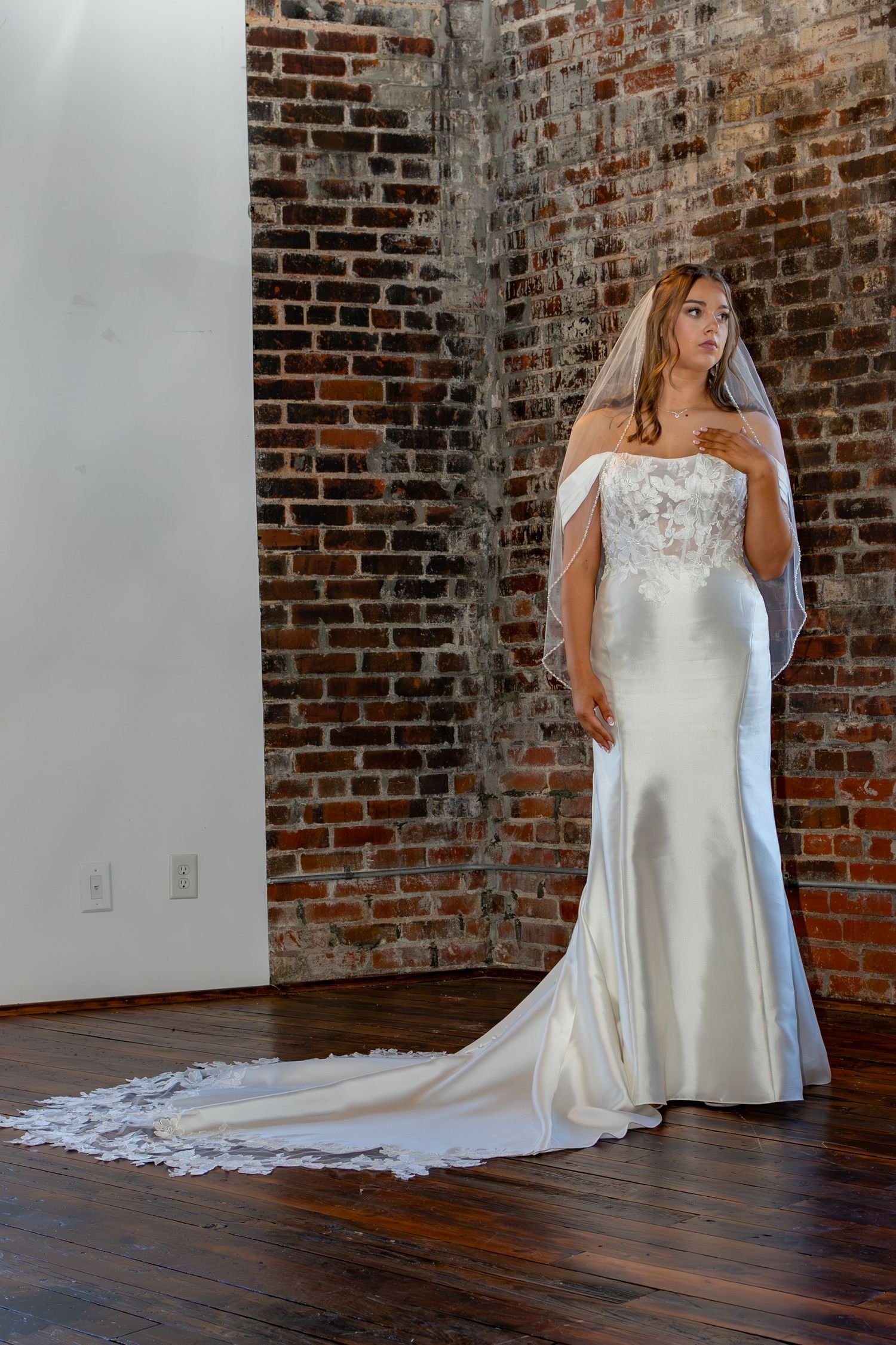 Wedding dress with strapless silhouette and sweeping train photographed in rustic brick studio with hardwood floors.