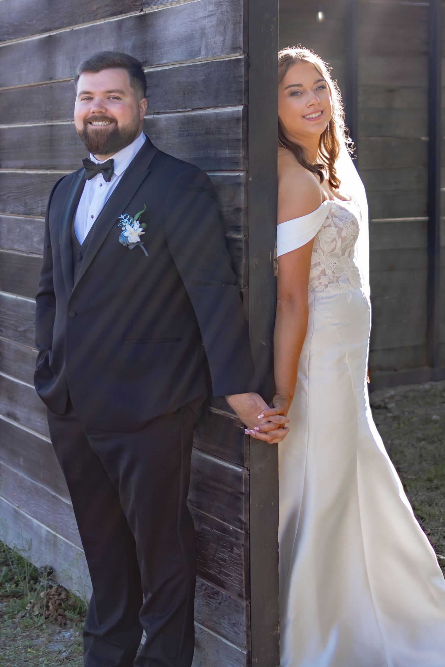 A newly married couple poses together against a rustic wooden wall for wedding photos in formal attire.