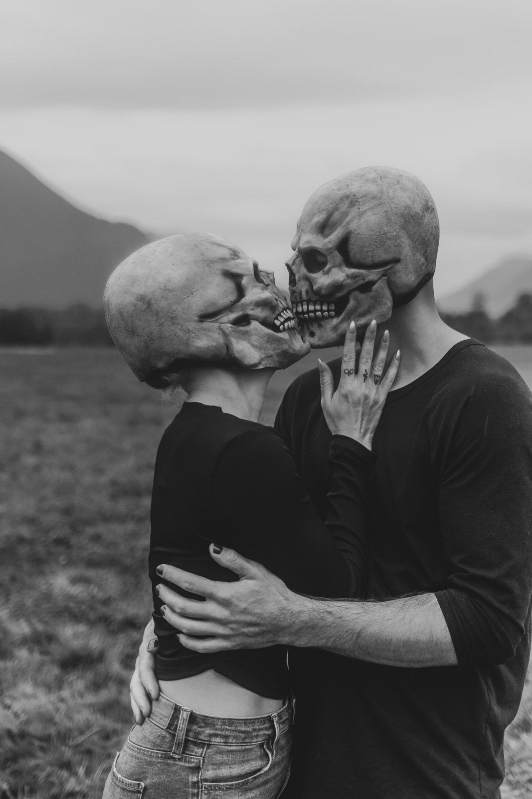 spooky Halloween couples photo shoot and woman kissing while both wearing skull mask in a foggy field and mountain background, spokane photo